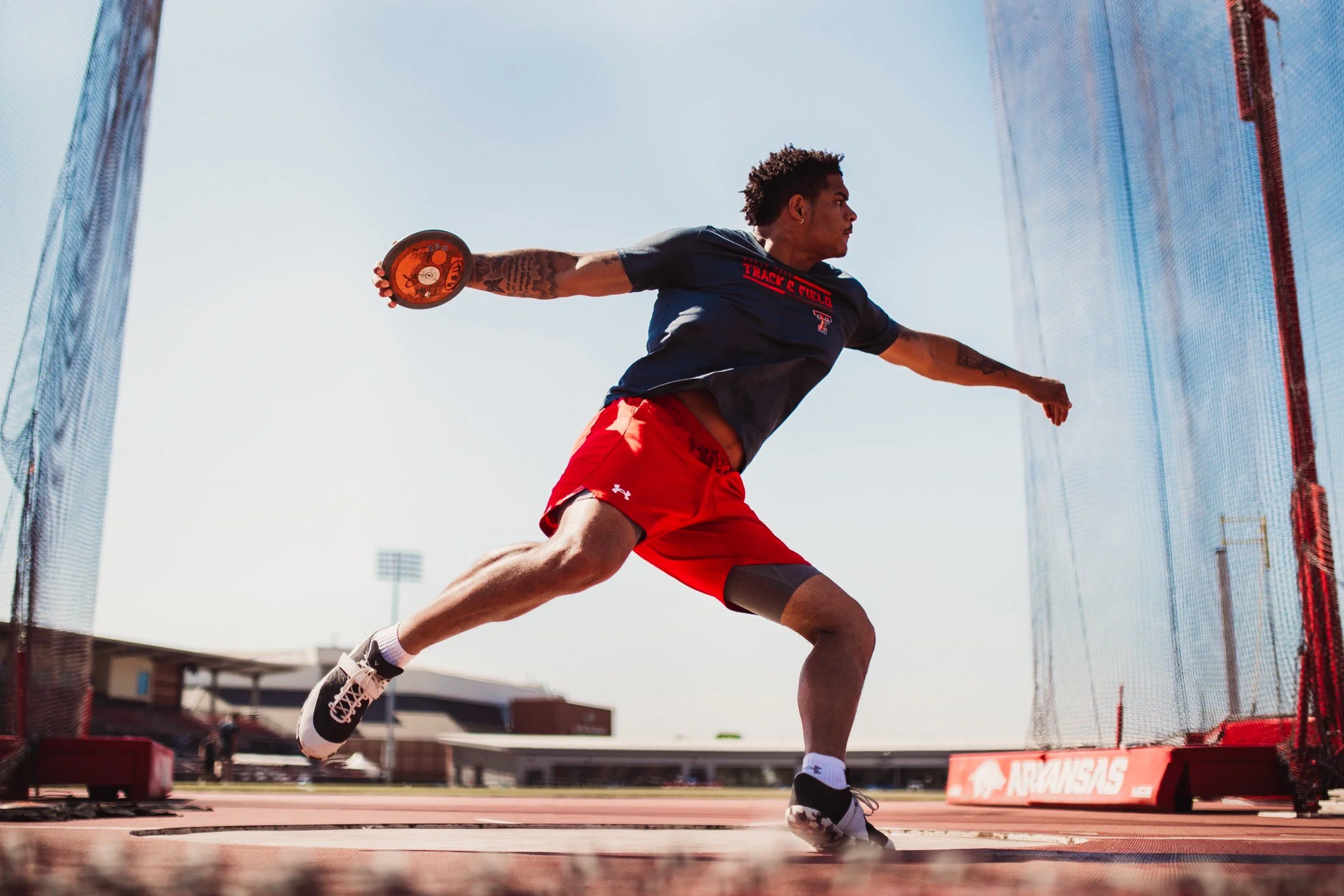 A male athlete throwing discus on a track field with a blue sky background.