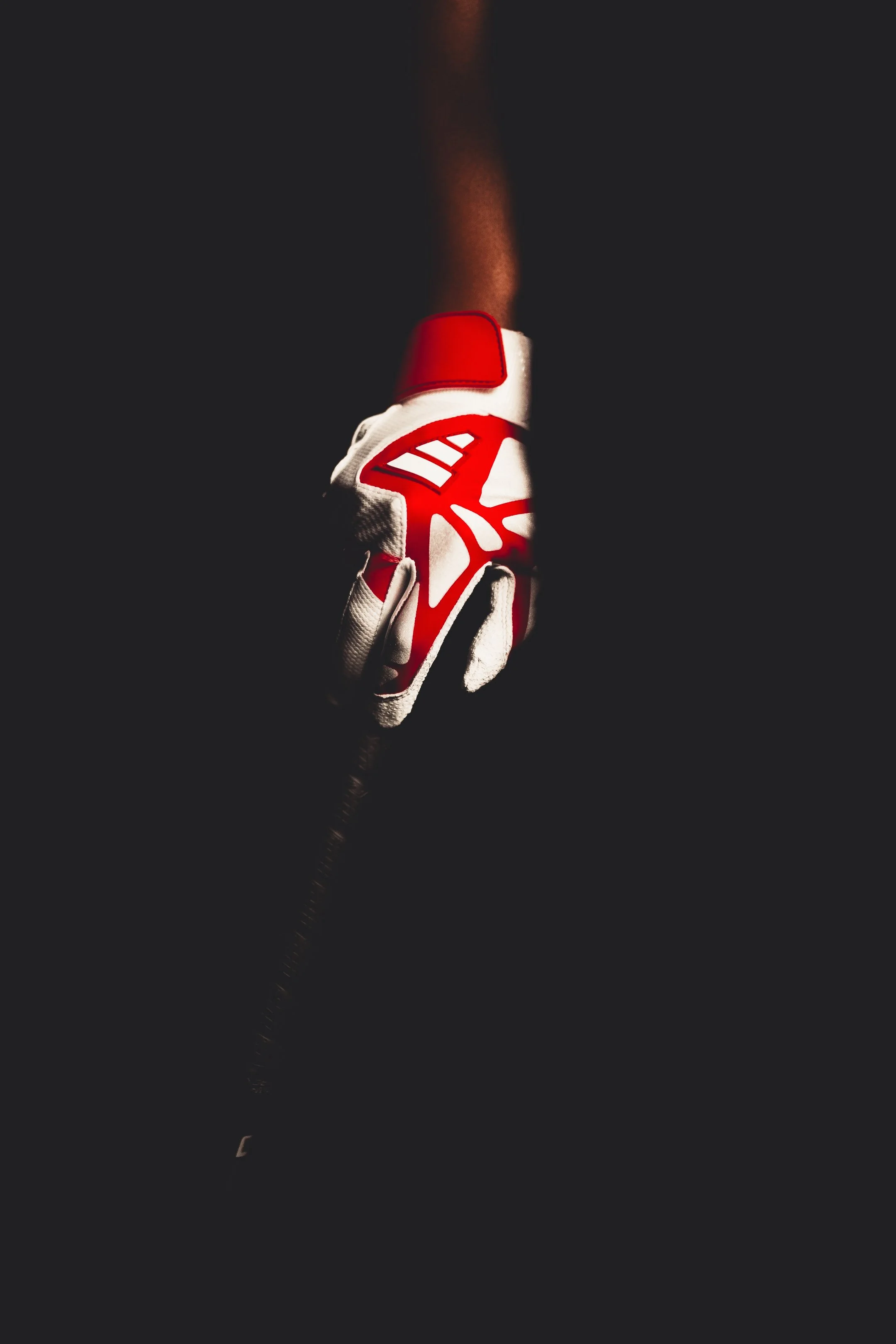 A close-up of a red and white athletic glove gripping a dark object against a dark background.