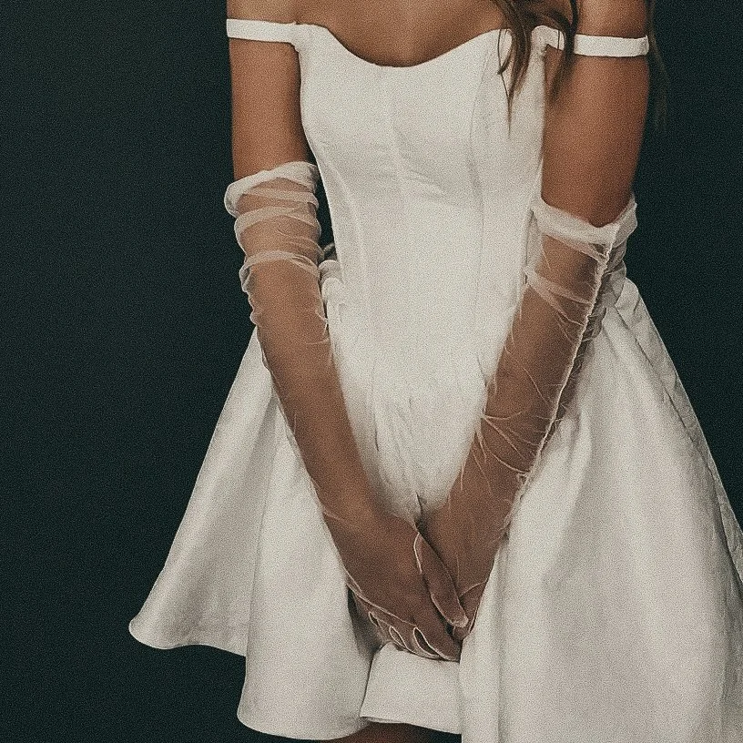 A woman in a white off-shoulder dress with sheer gloves.