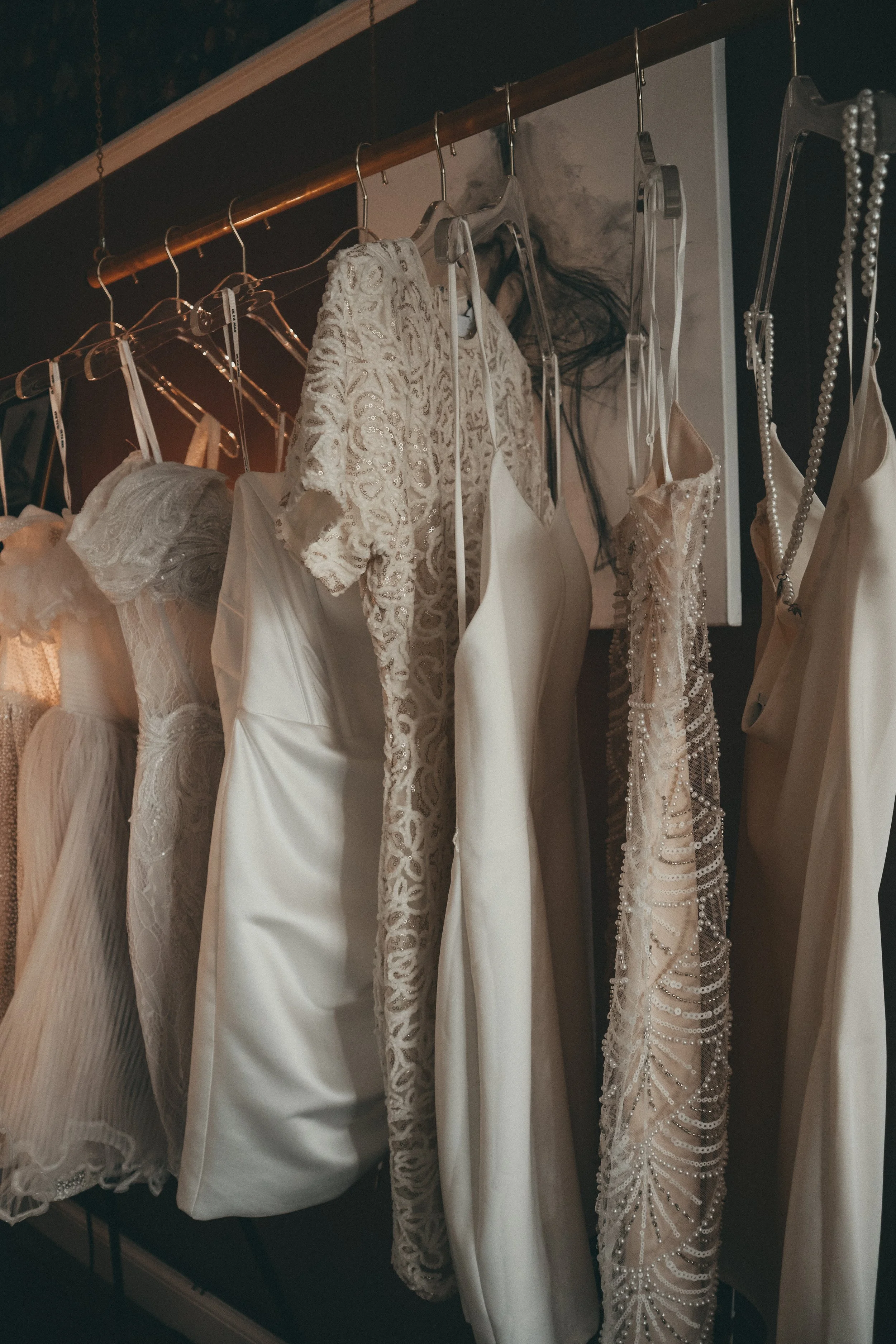 A collection of wedding dresses hanging on a clothing rack, with various lace, pearl, and satin fabrics.