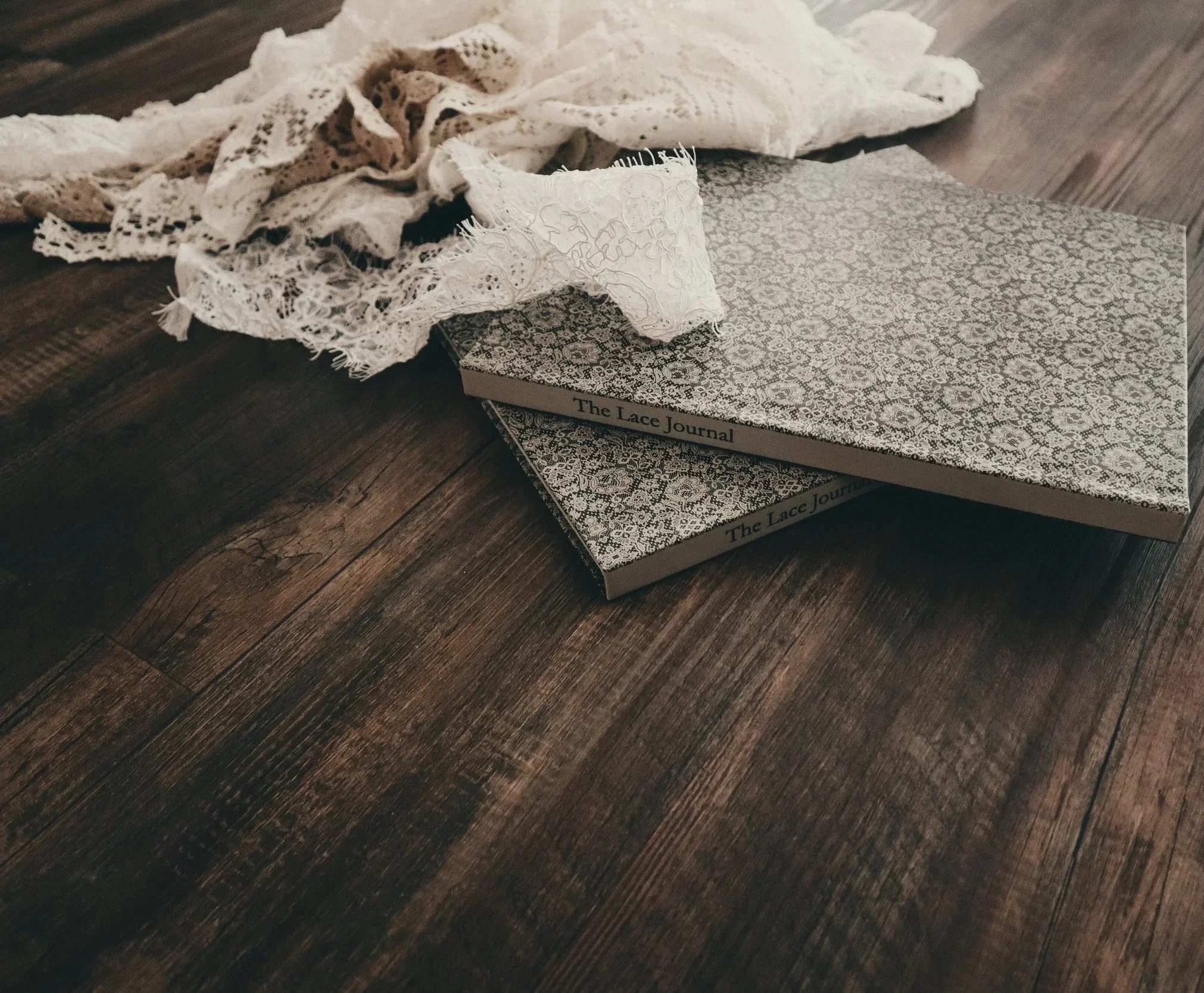 A lace journal with a patterned cover, placed on a wooden surface, with some lace fabric draped over it.