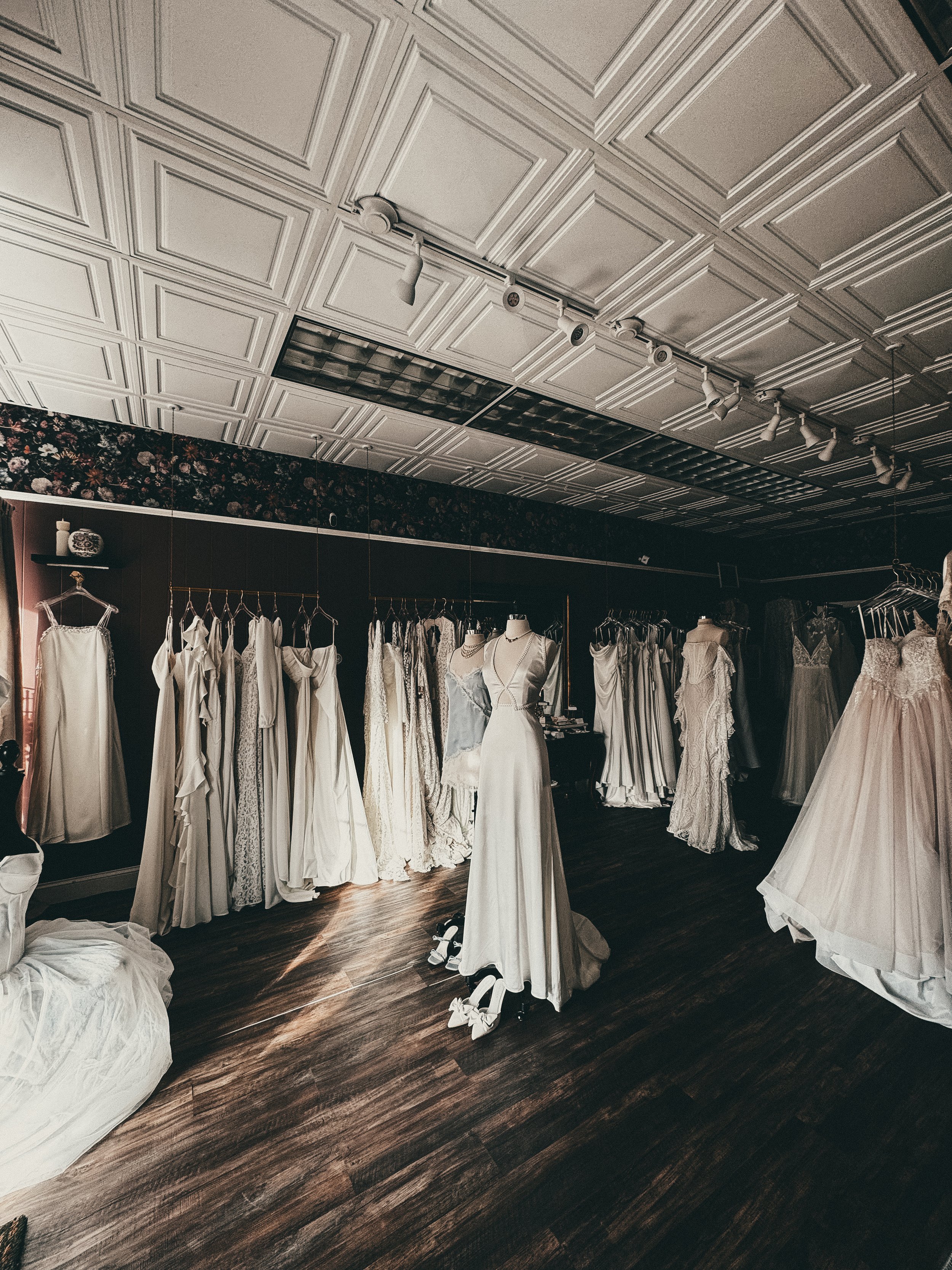Inside the Art & Lace bridal studio — beneath tin ceilings and dark floral wallpaper, a curated rack of internationally designed wedding gowns is displayed for private appointments.