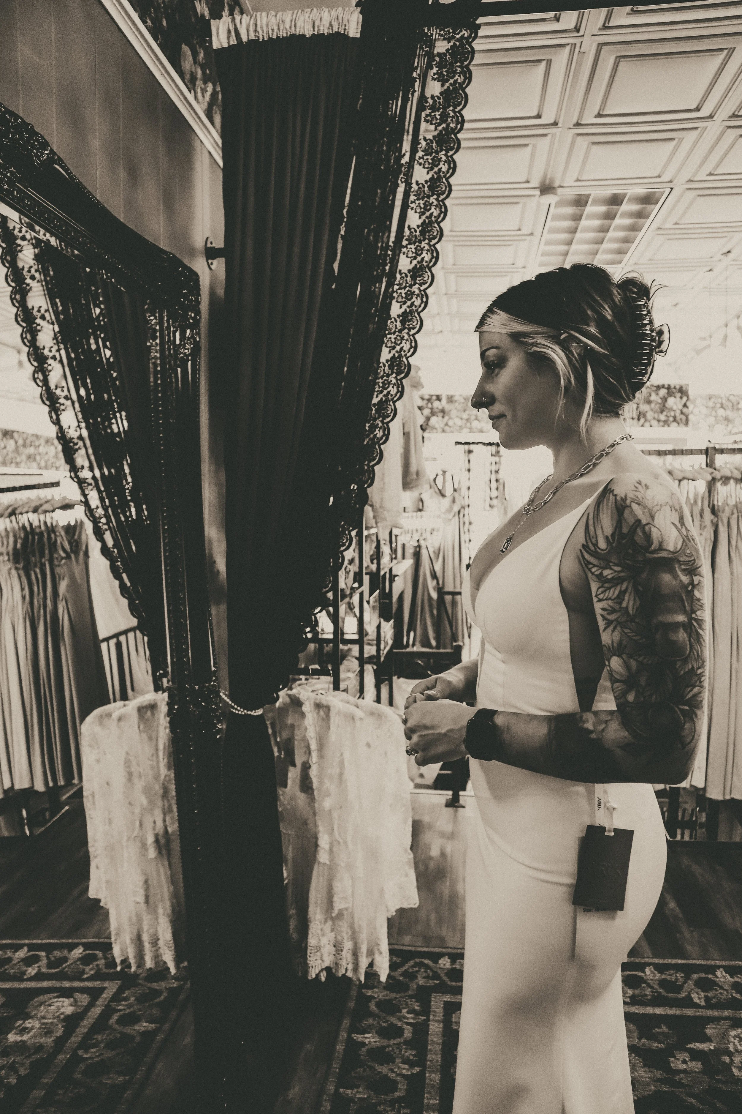 Woman with tattoos in a dress looking at herself in a mirror inside a store
