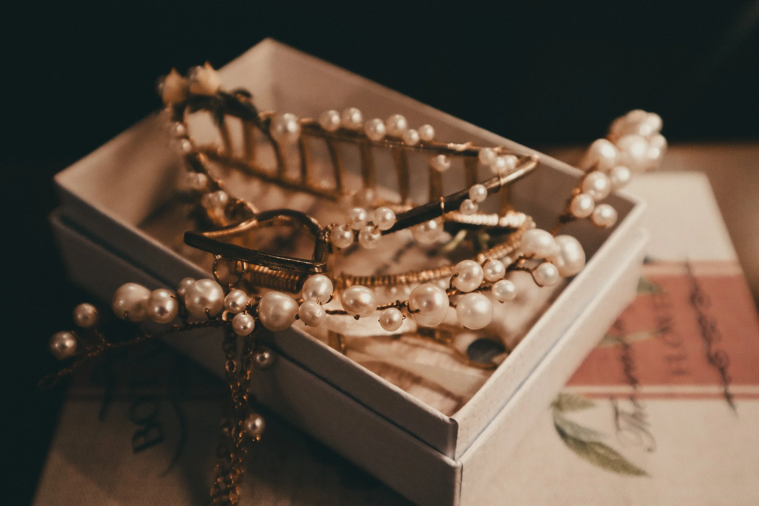 A jewelry box with pearl necklaces and bracelets, some with gold chains, inside a floral-patterned box.