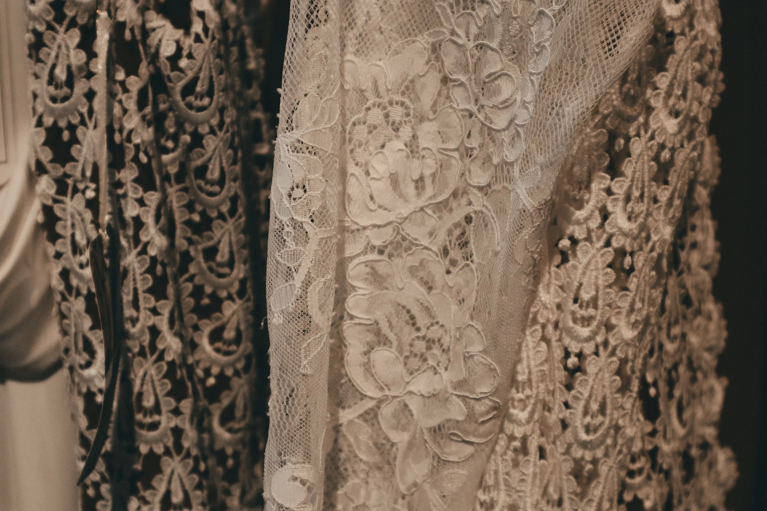 Close-up of intricately embroidered lace fabric, likely part of a wedding or vintage dress, featuring floral patterns and delicate details.