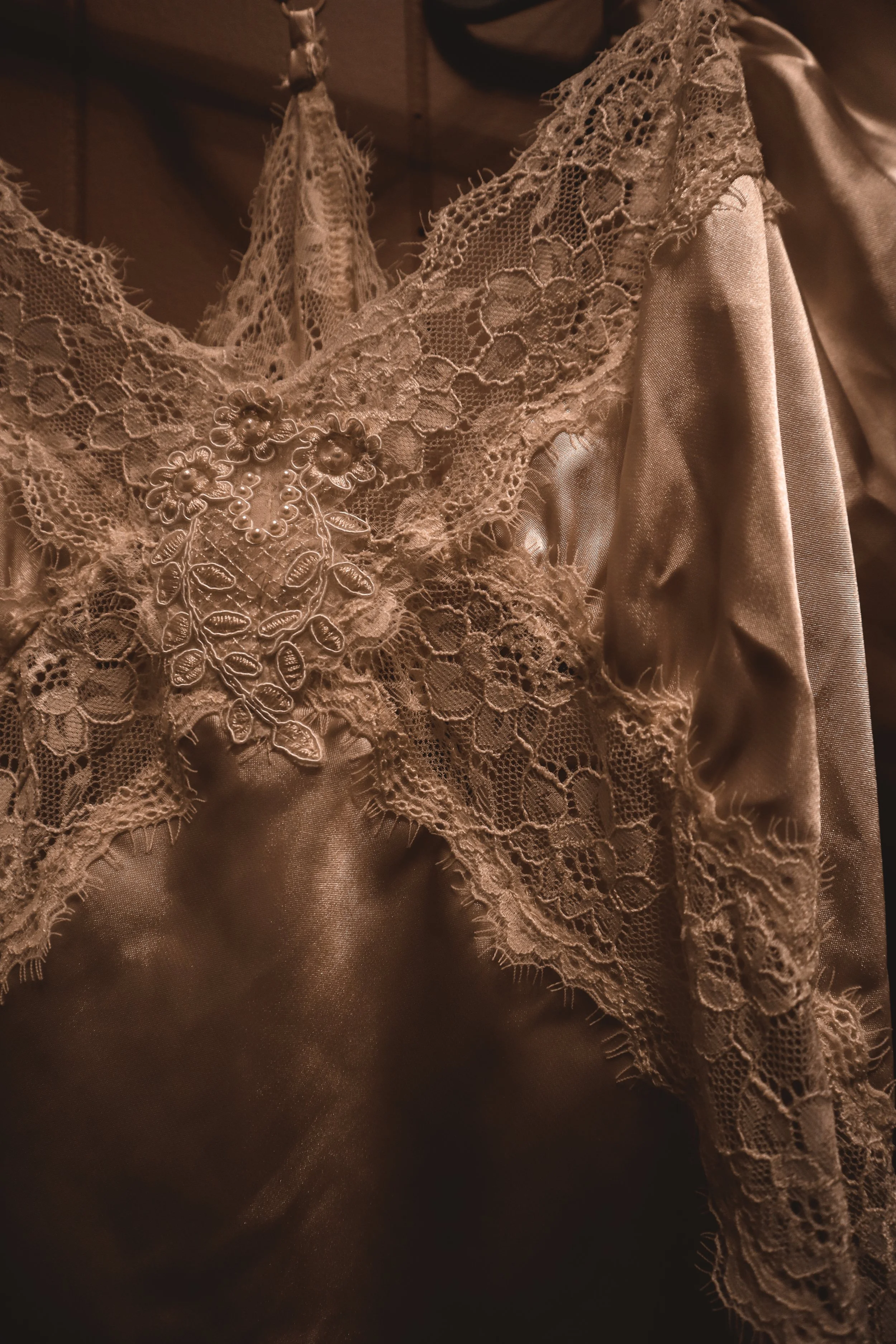 Close-up of a vintage lace dress with pearl embellishments and floral embroidery, made of shiny satin fabric.