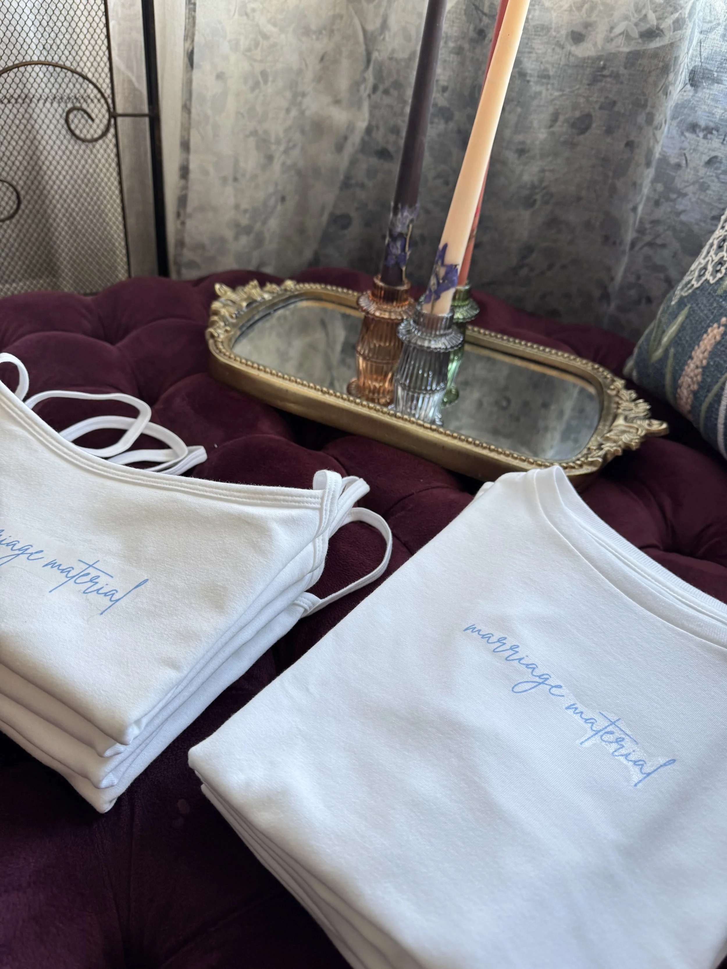 The Marriage Material Tee folded on a burgundy velvet ottoman — an Art & Lace signature merch piece
