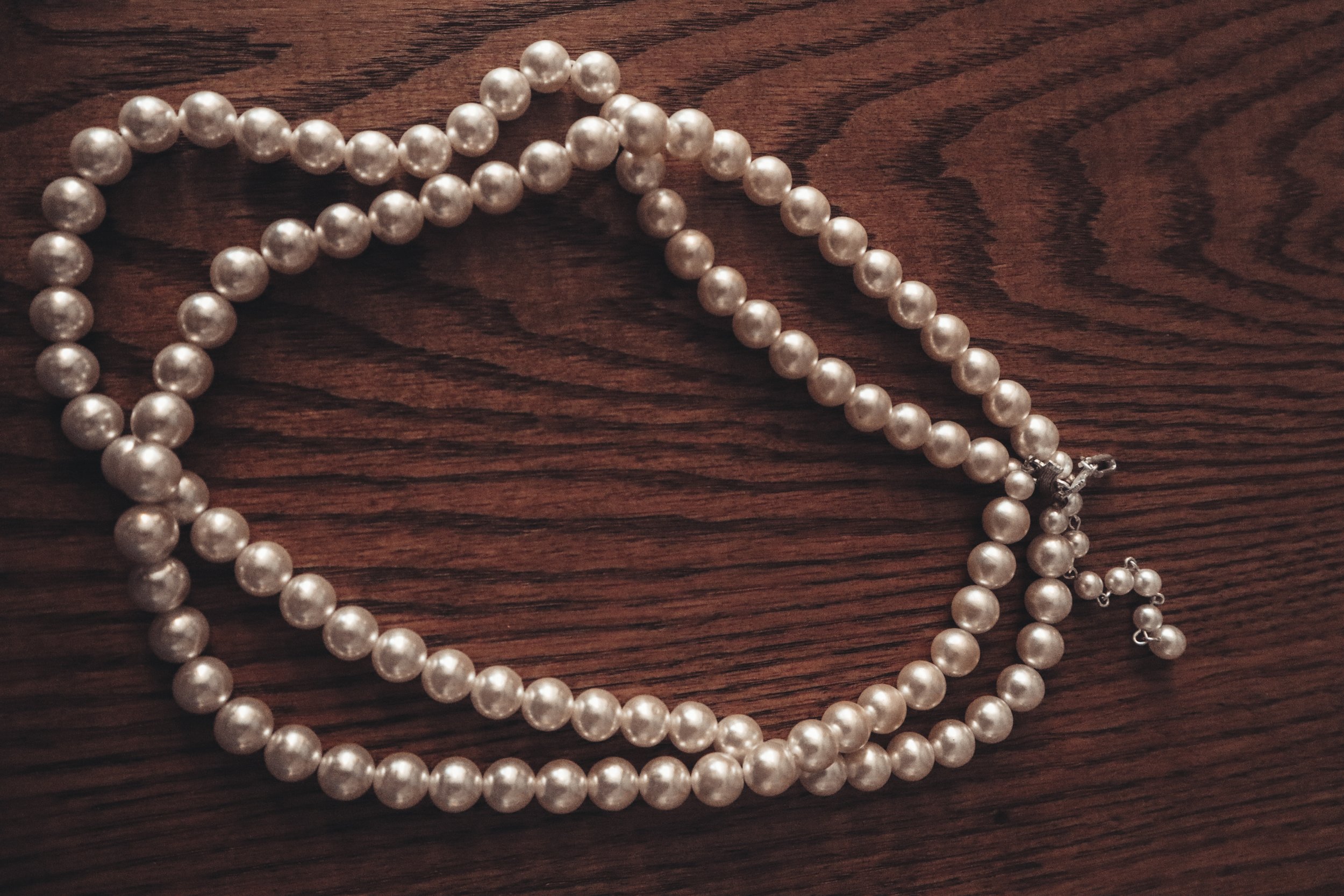 Two pearl necklaces on a dark wooden surface.