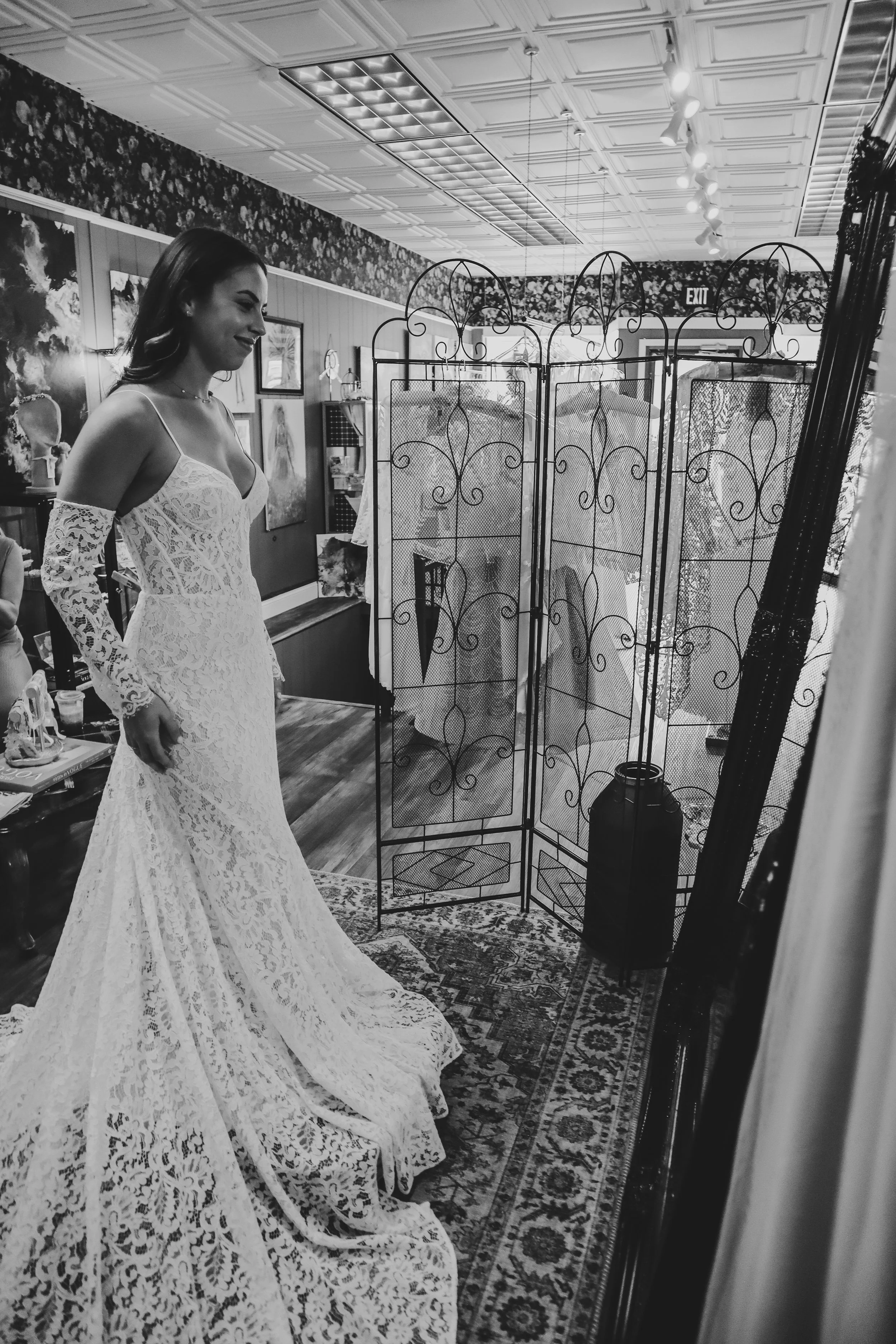 A woman in a detailed lace wedding dress trying on a wedding gown in a boutique fitting room.