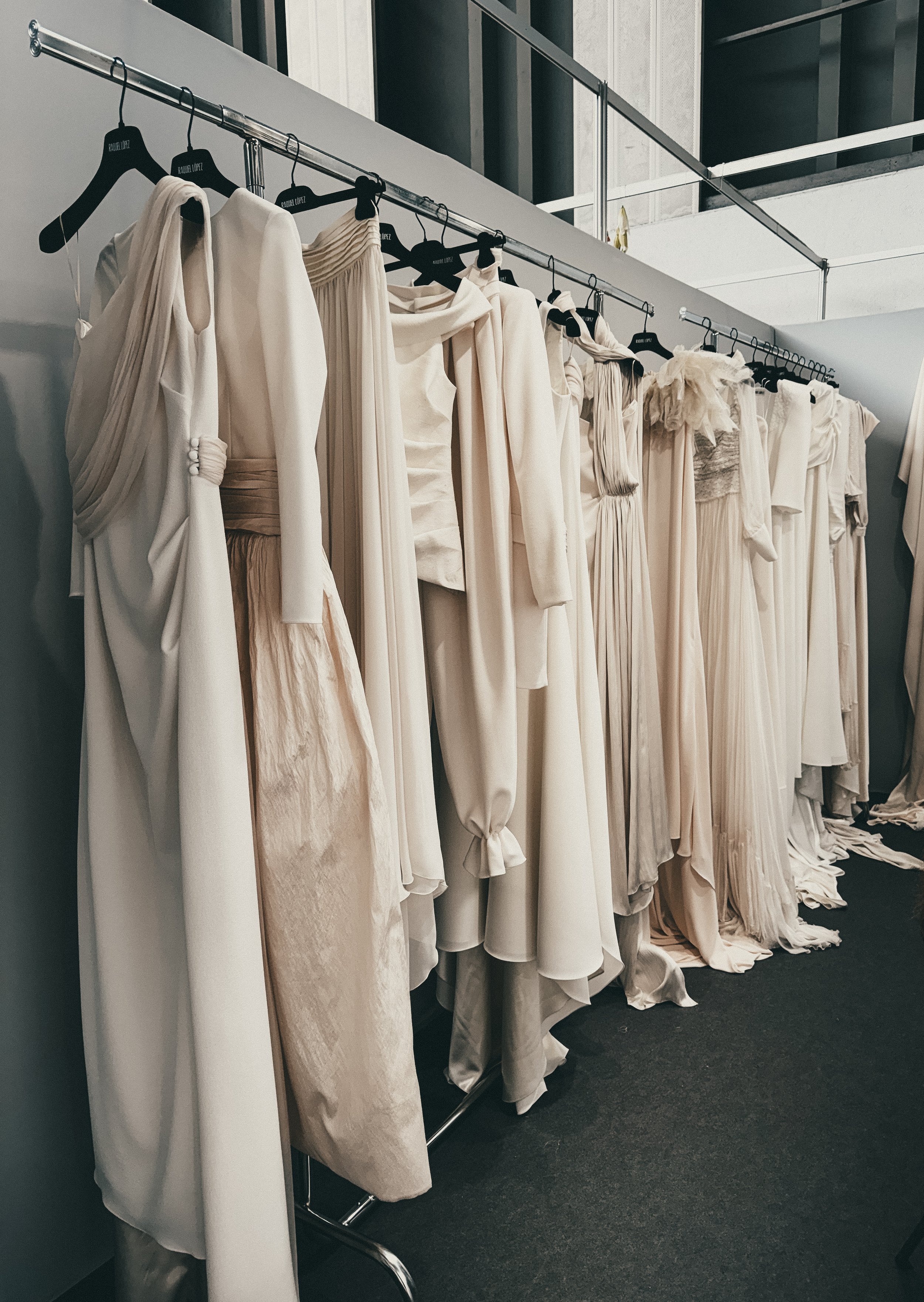 Cream-colored and white dresses hanging on a clothing rack in a fashion studio or backstage area.