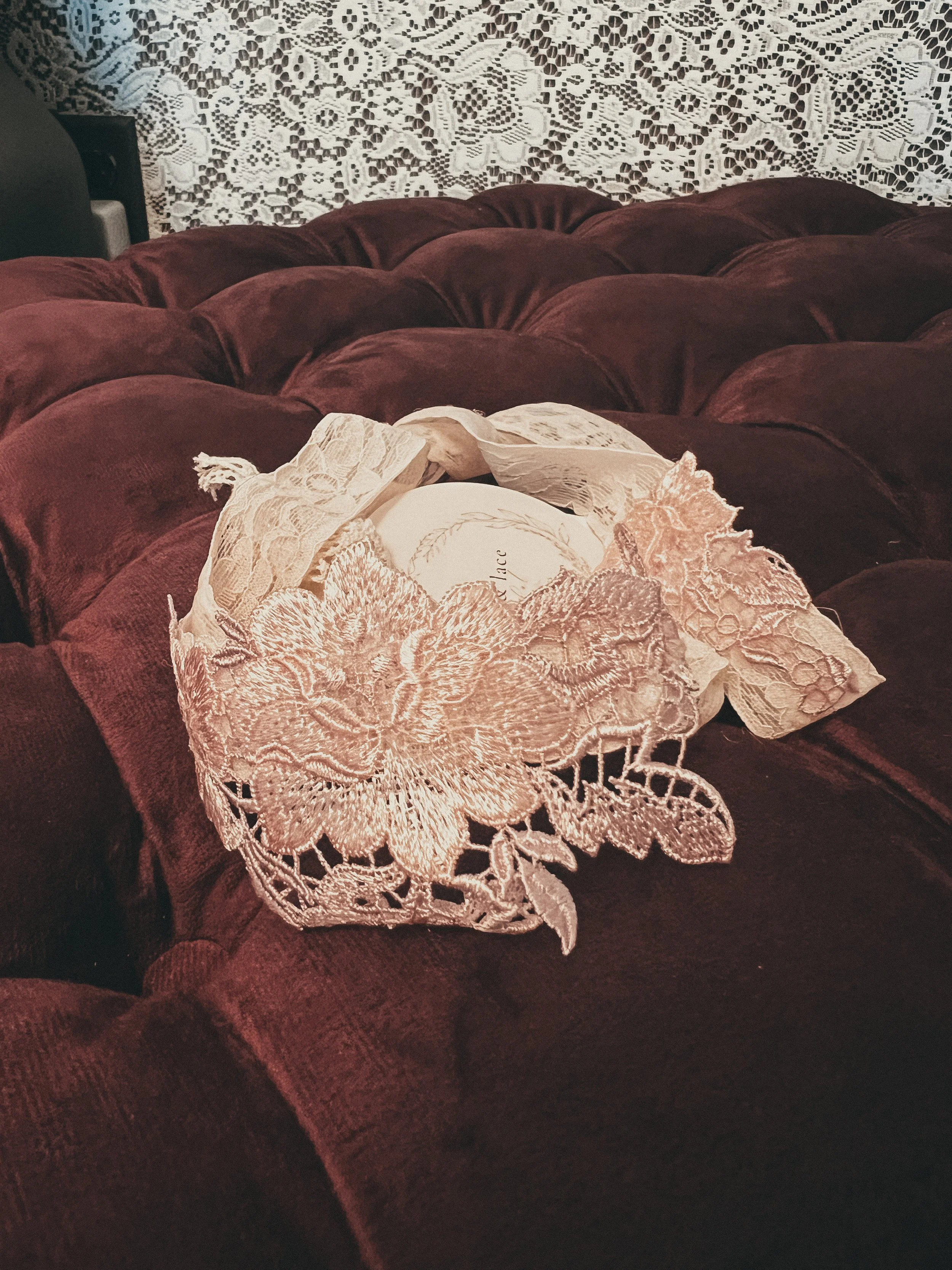 Pink Floral Lace Bridal Garter — a delicate blush-pink lace garter styled on a burgundy velvet ottoman