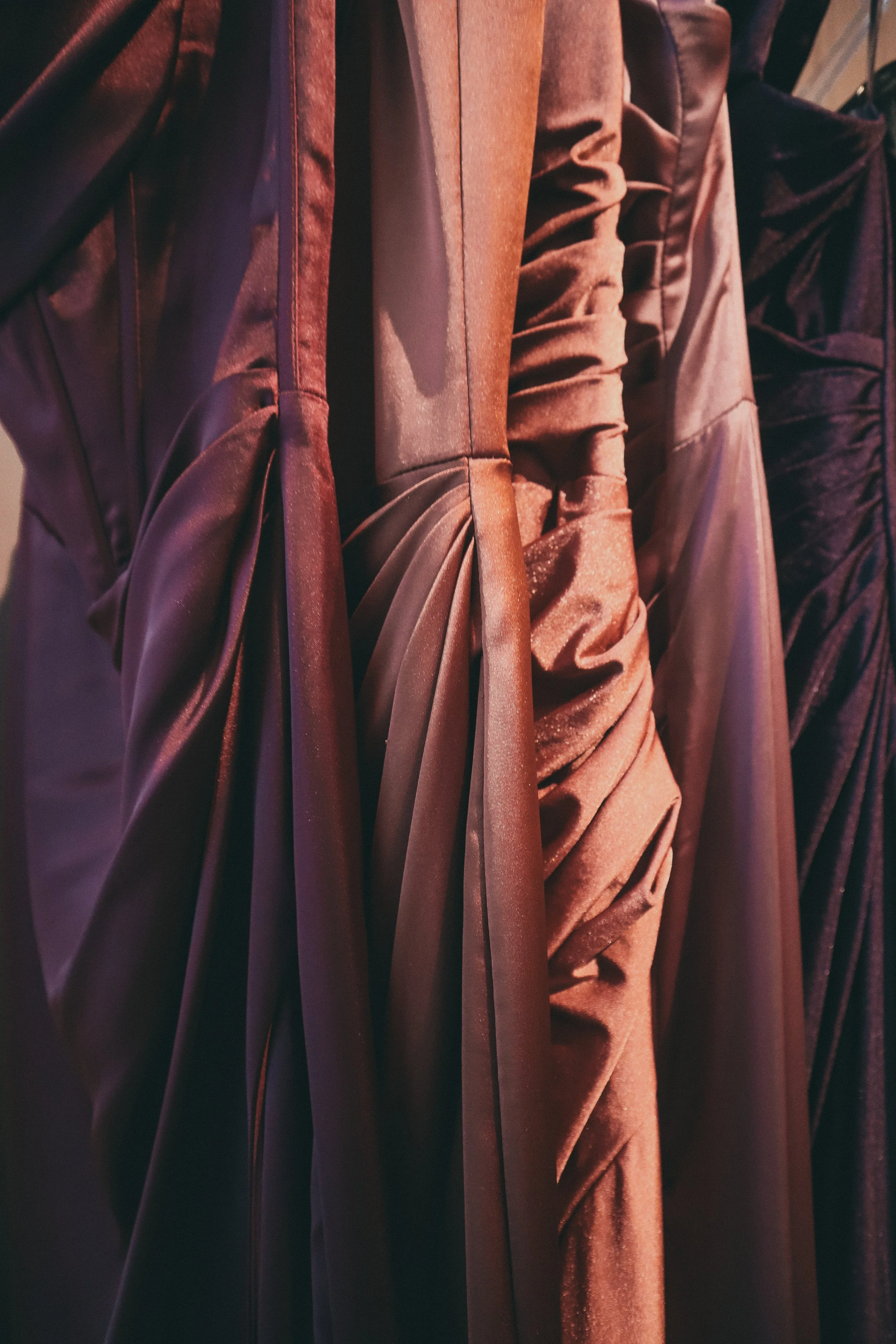 Close-up of several dresses in shades of brown and burgundy, featuring draped and ruched fabric.