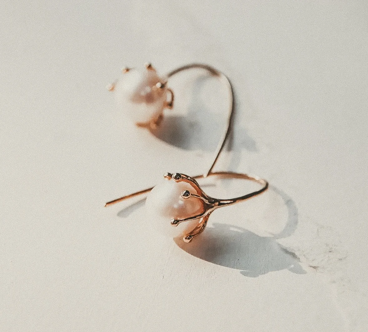 A pair of earrings shaped like hearts with a pearl and metallic finish, placed on a white surface.