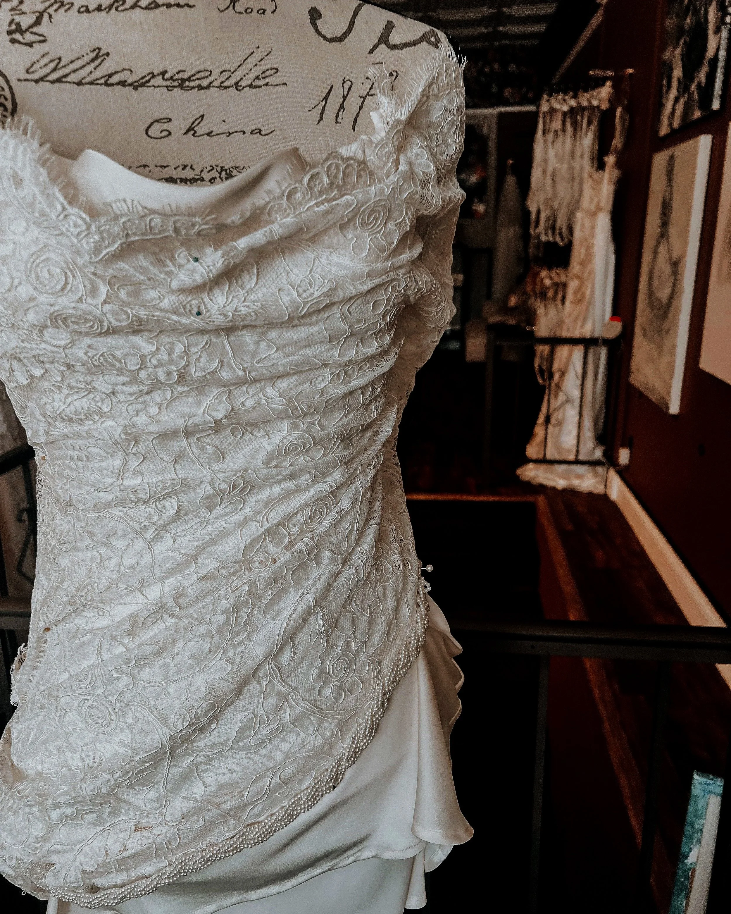 Close-up of a vintage white wedding dress with detailed embroidery, displayed on a mannequin in a boutique or atelier.