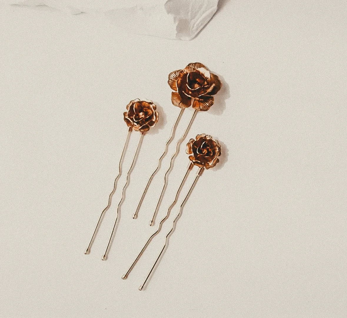 Four hairpins with metallic rose-shaped decorations on a white surface.