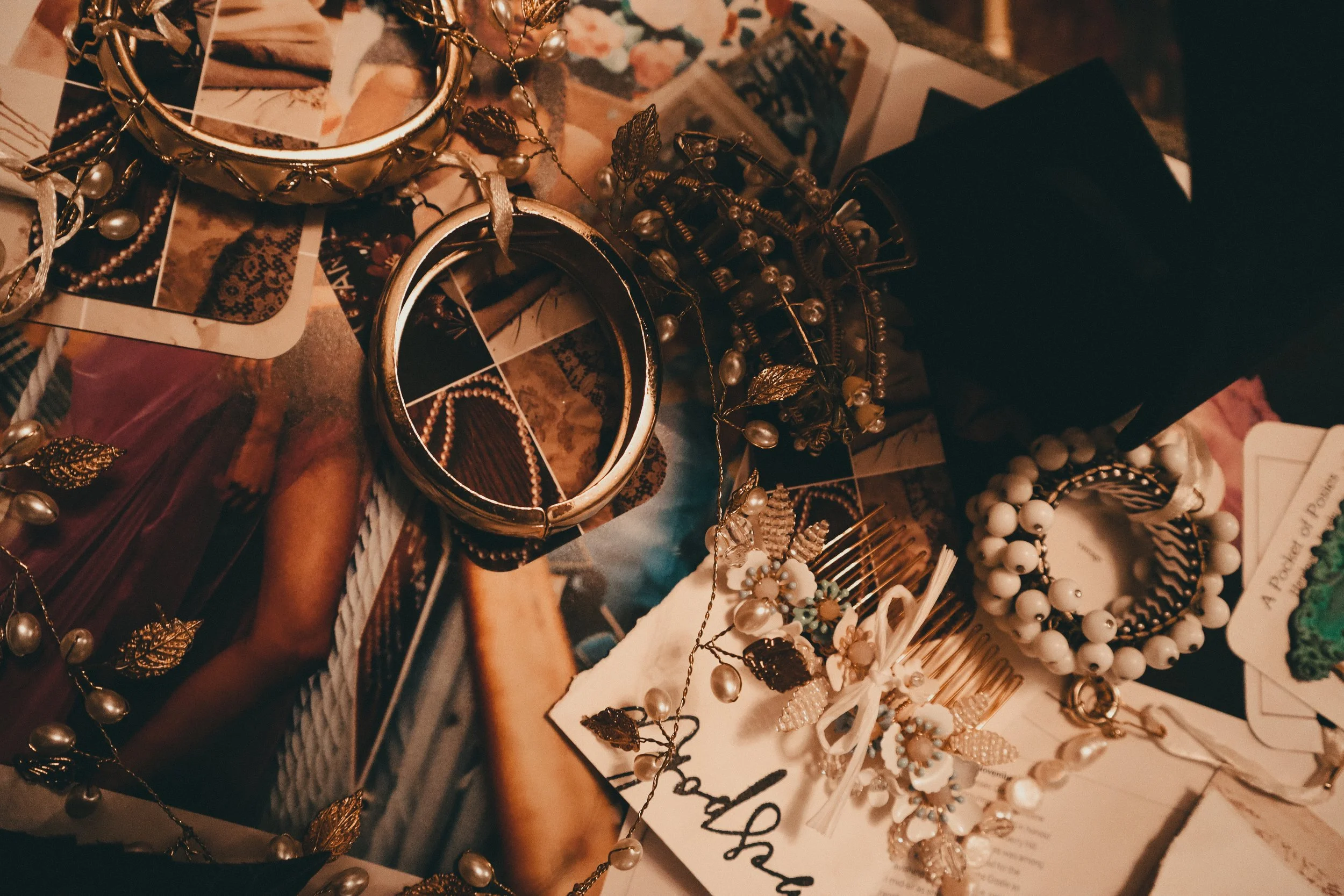 A collection of jewelry including pearl and gold bracelets, hair accessories, and cards on a vintage magazine.