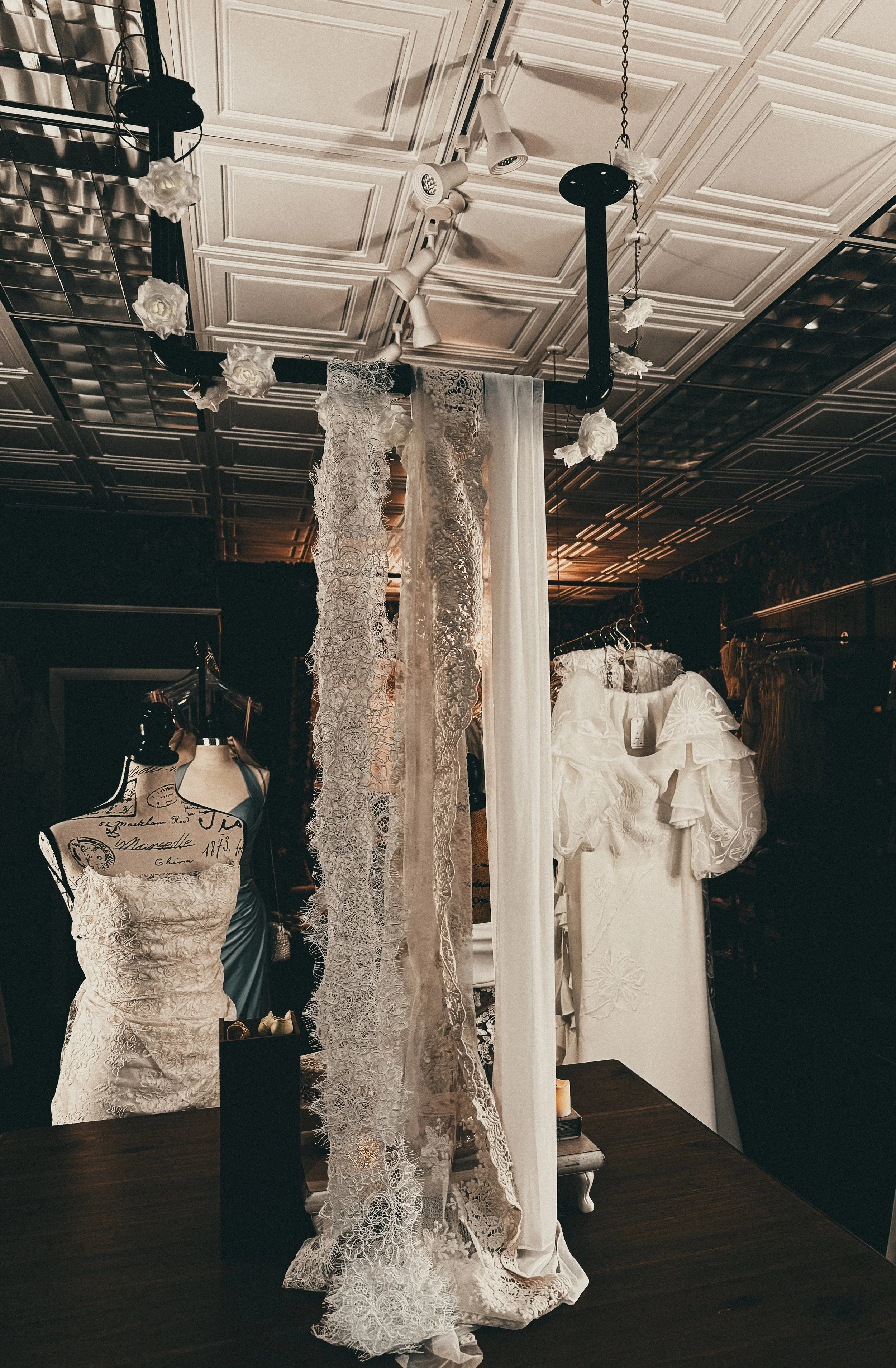 Display of white wedding dresses and laced fabric trims in a boutique fitting room.