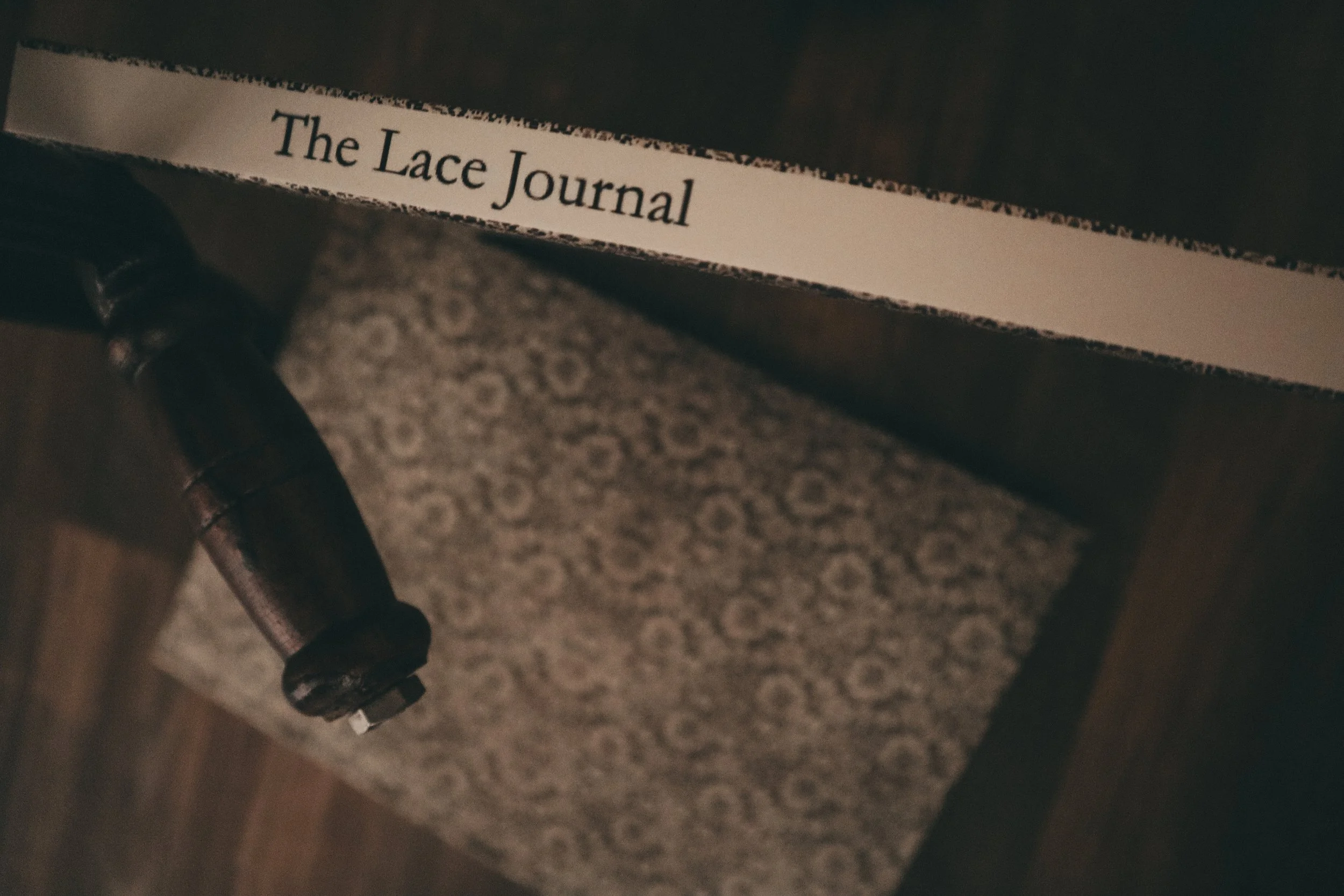 Close-up of a dark leather chair with a piece of paper that reads 'The Lace Journal' underneath the chair leg.