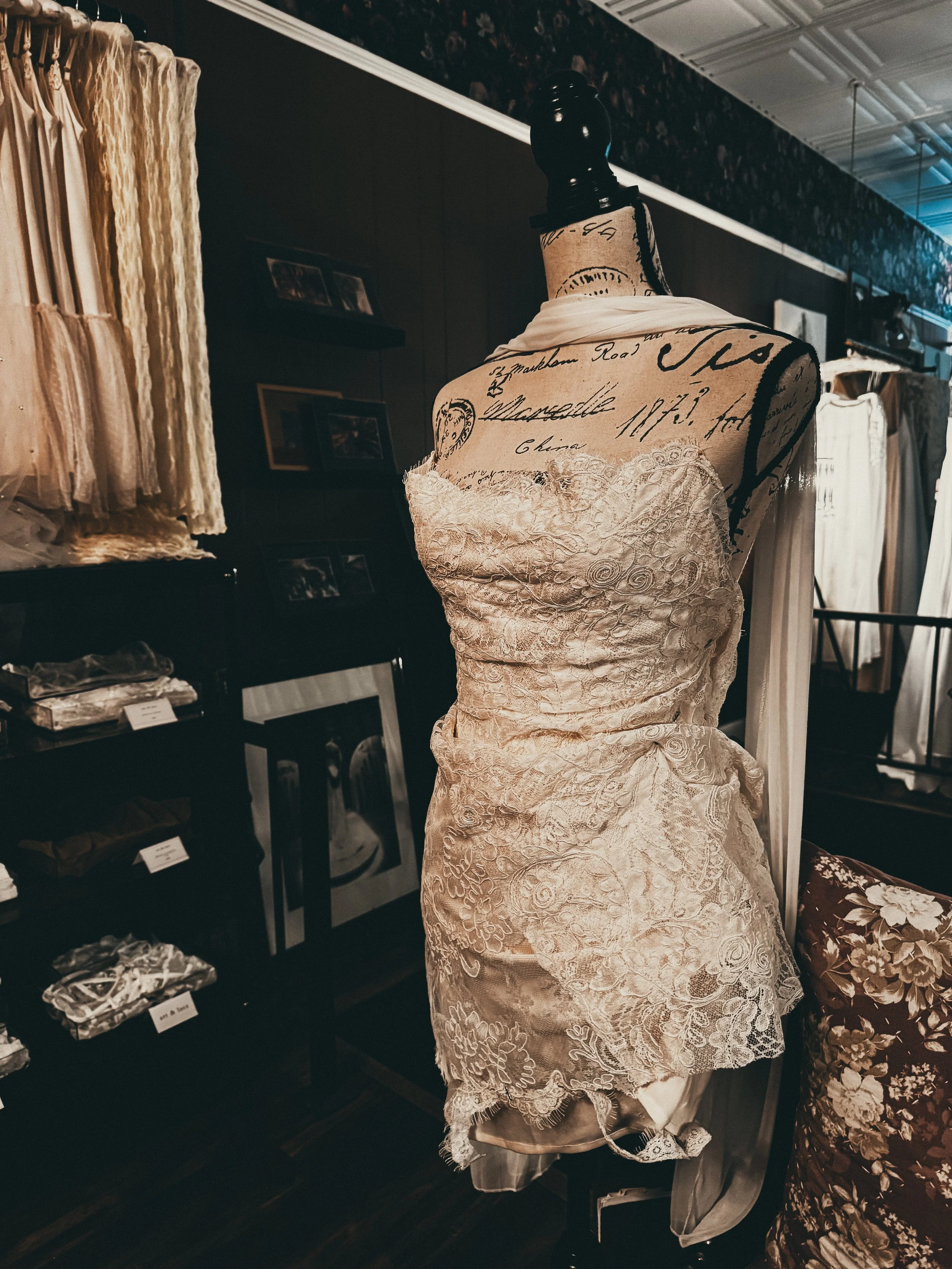 Bespoke heirloom mini bridal gown in lace and satin on a vintage dress form — The Atelier signature at Art & Lace Bridal.