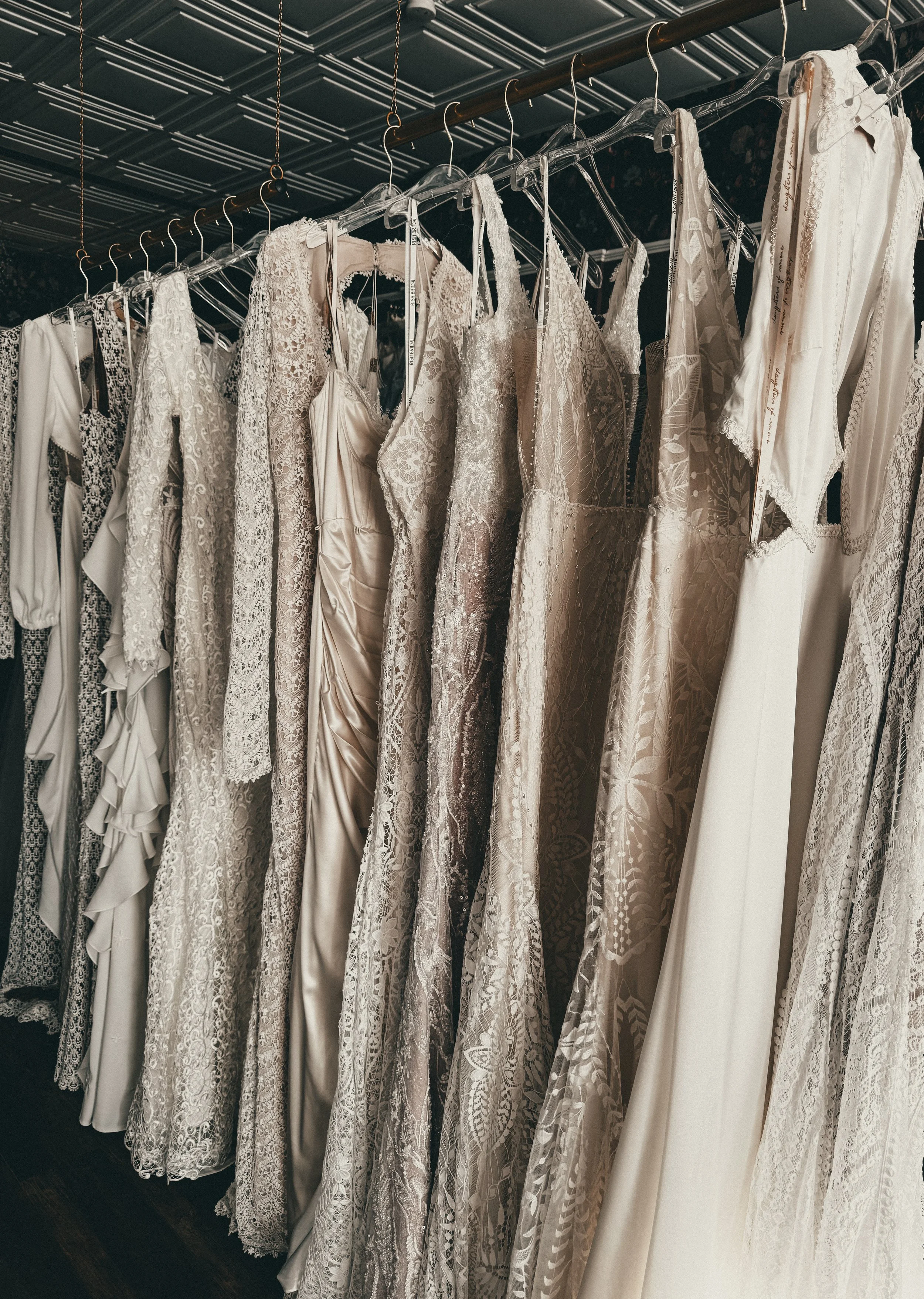 Rack of vintage bohemian wedding gowns under tin ceilings at Art & Lace Bridal — Boho realm styling in Massachusetts.