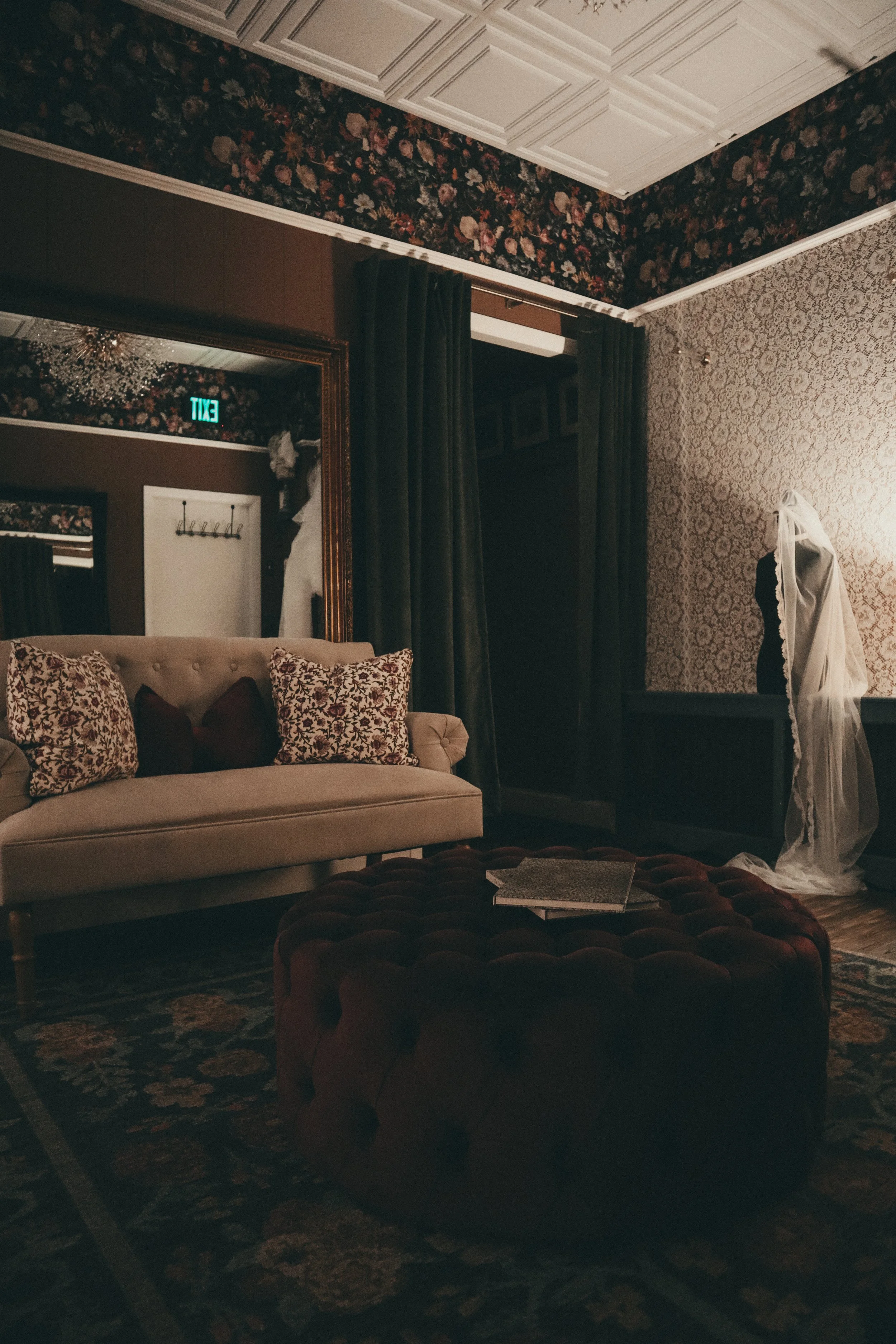 The try-on sanctuary at Art & Lace Bridal — a floral-wallpapered room with a soft sofa, tufted ottoman, and gilded mirrors for private appointments.