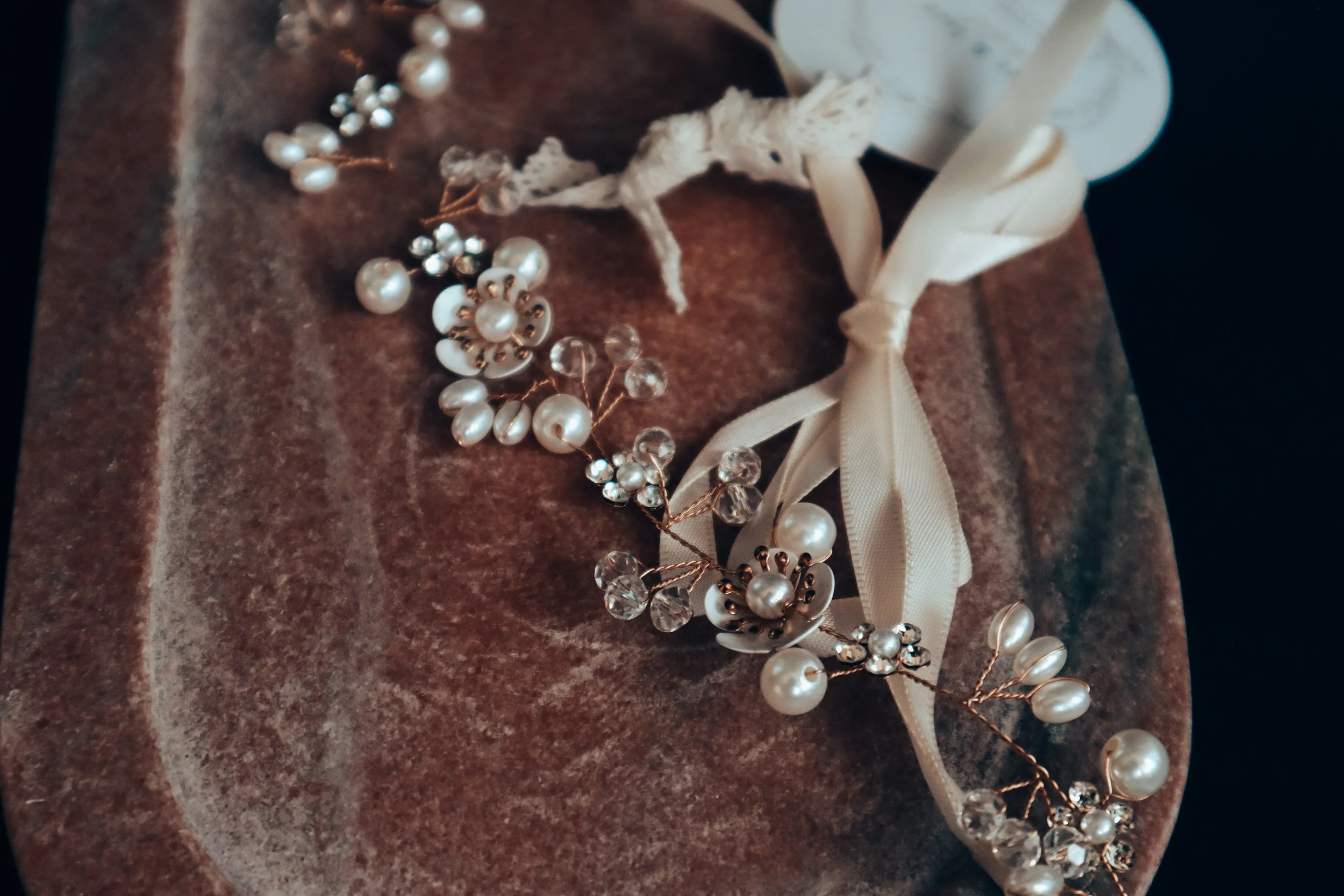 Pearl and crystal decorative hair accessory with cream ribbon tied in a bow on a textured brown surface.