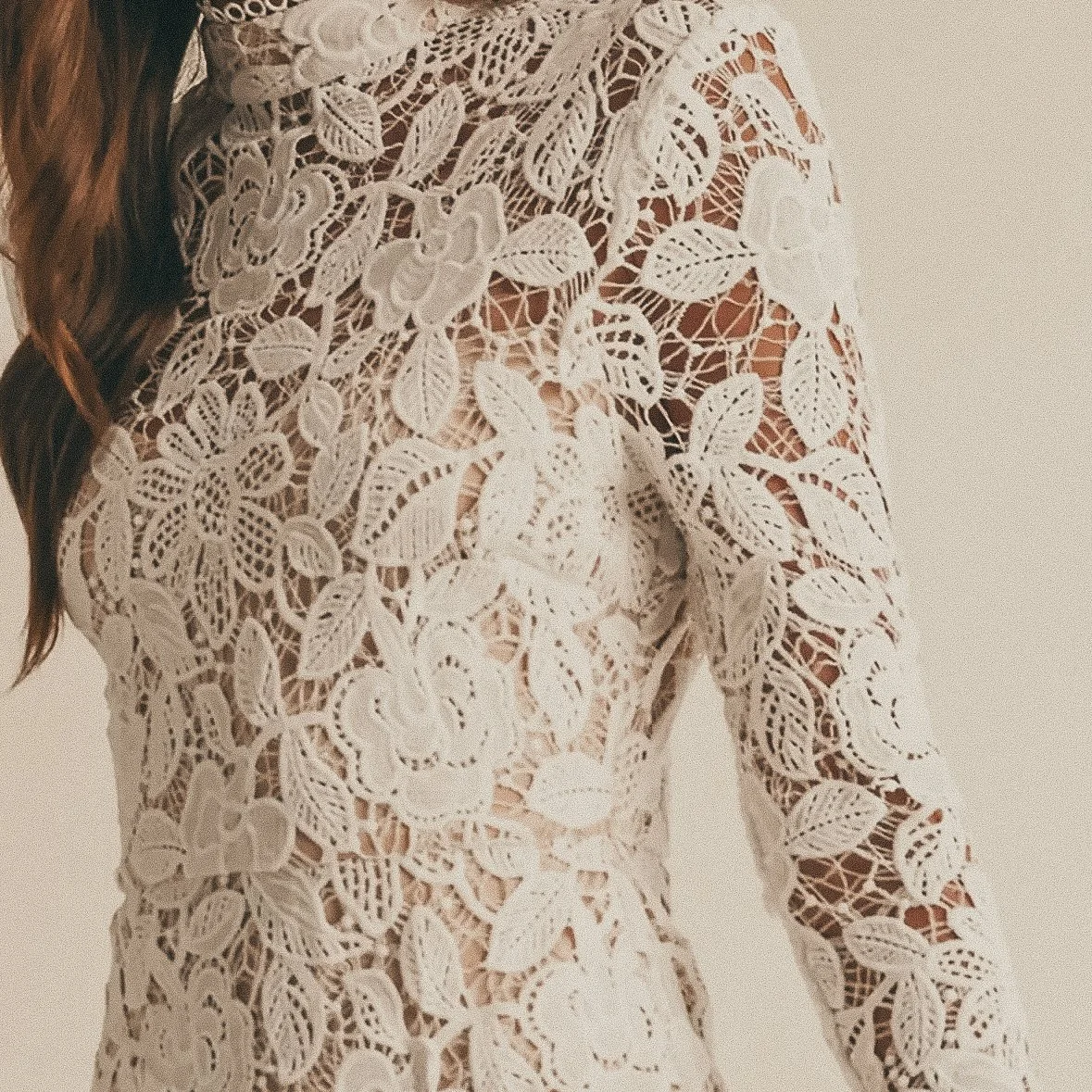 Close-up of a woman wearing a white lace dress with floral patterns and intricate leaf designs.