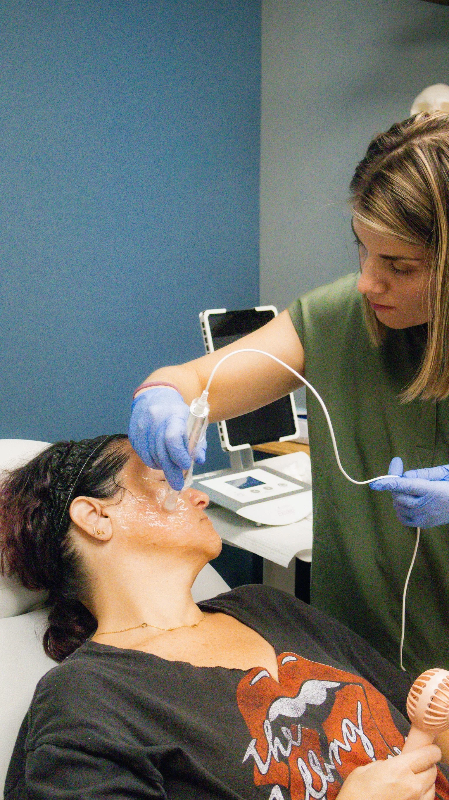 A woman receiving a facial treatment with a skincare device applied by a professional wearing gloves in a spa setting.