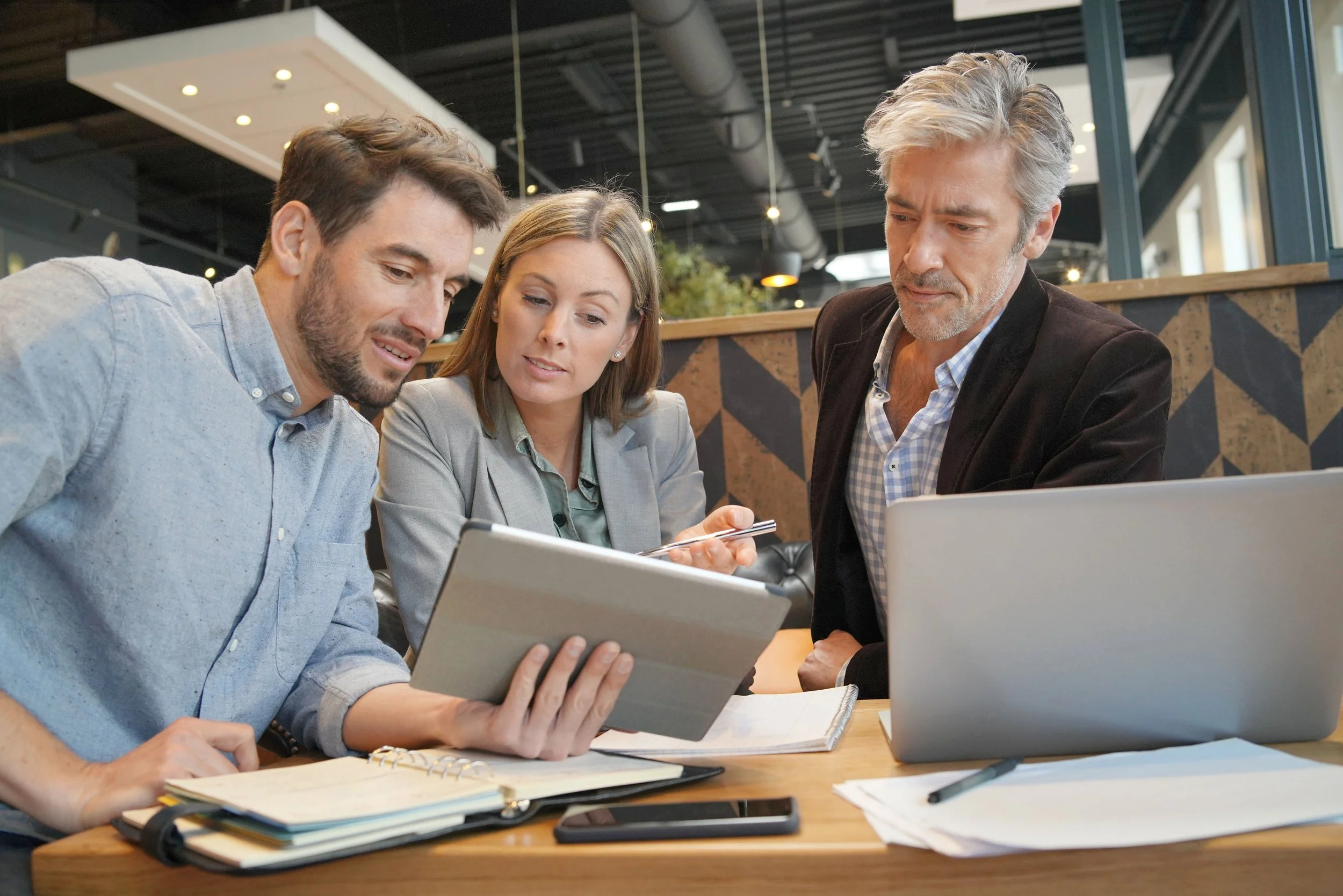 3 people sitting looking a handheld computer