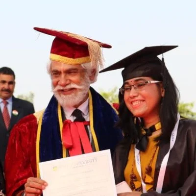 An elderly man and a young woman in graduation caps and gowns smiling and holding a diploma, celebrating graduation outdoors.