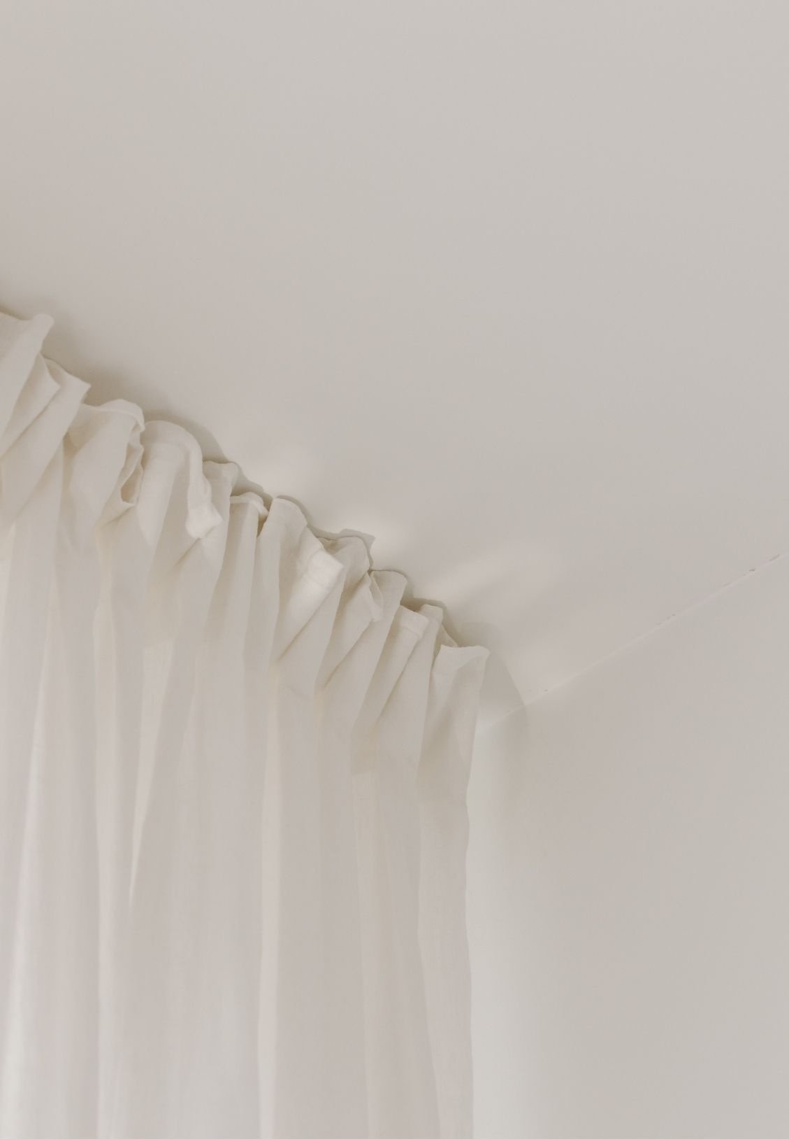 Close-up of white curtains hanging from a curtain rod against a white ceiling.