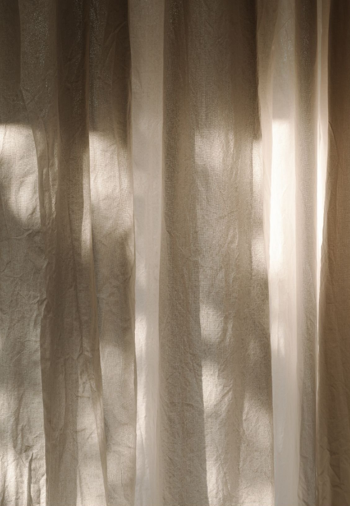 Light-colored sheer curtains hanging with sunlight filtering through.
