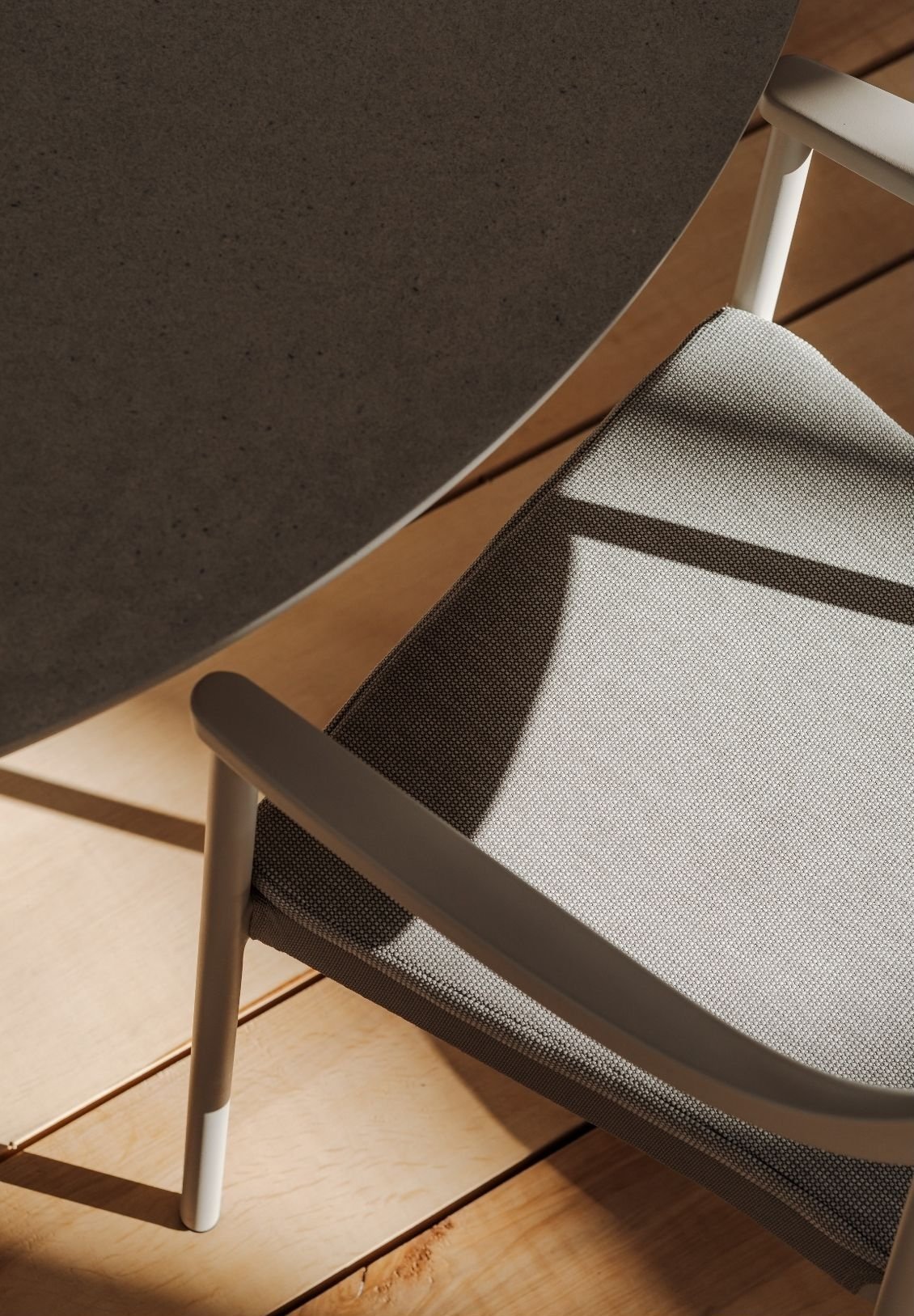 Top-down view of a gray chair with a speckled fabric seat and white metal armrest, positioned beneath a dark gray table on a wooden floor.