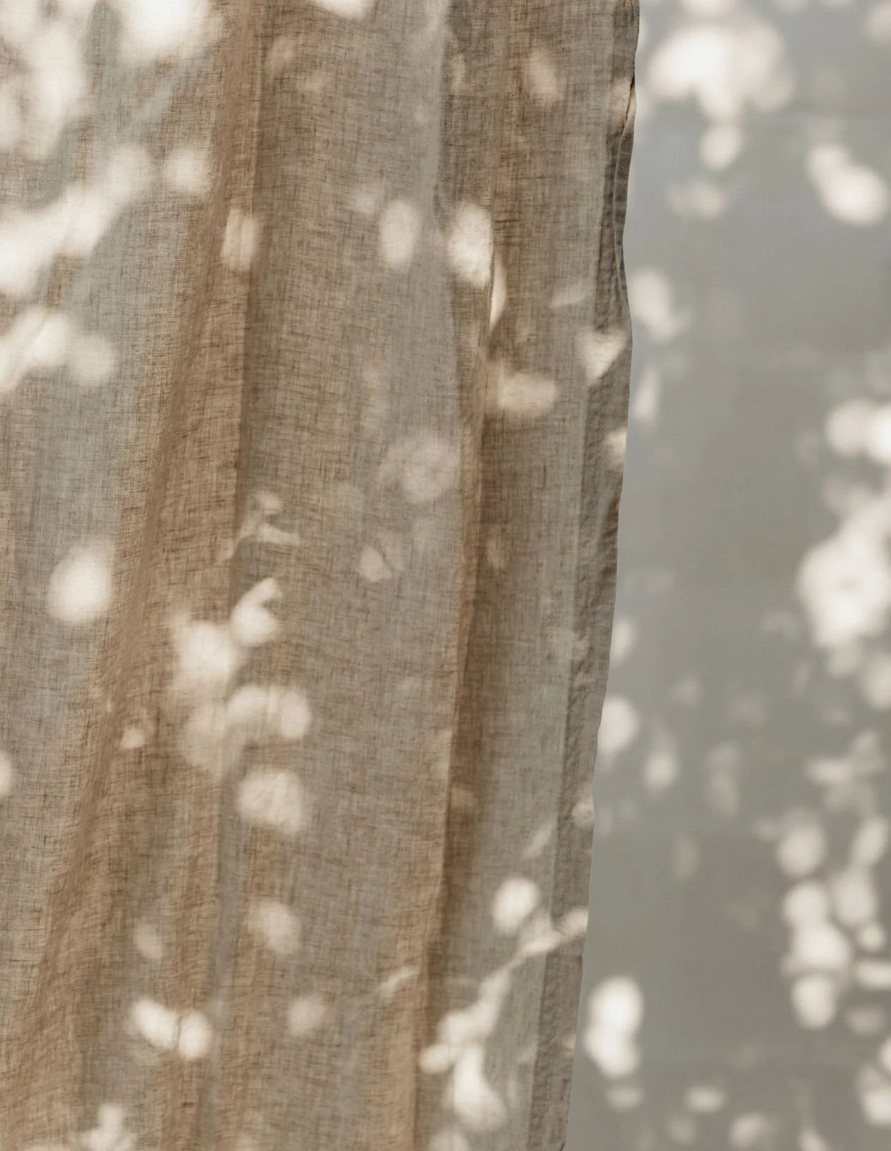 Close-up of a sheer, beige curtain with sunlight creating bokeh patterns on the fabric.