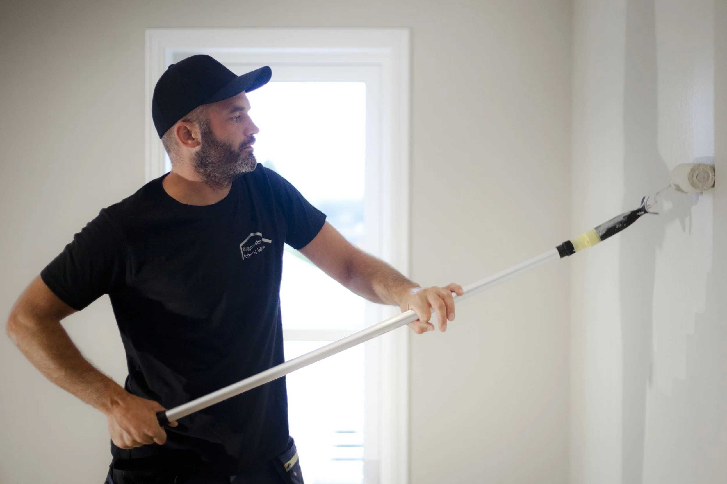 Mann som maler en vegg hvit med rullende malingsrull.