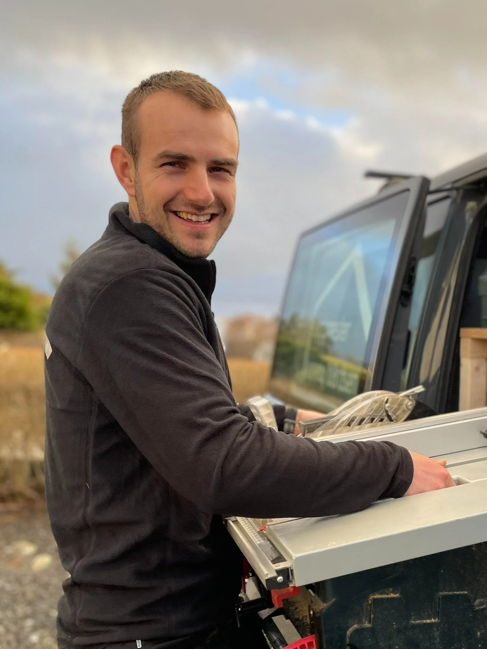 En mann smiler og jobber med en elektrisk sag utendørs