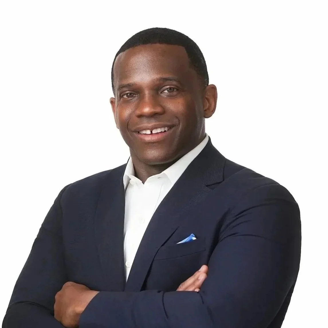 Professional portrait of a smiling Black man in a dark suit and white shirt, arms crossed, against a plain white background.