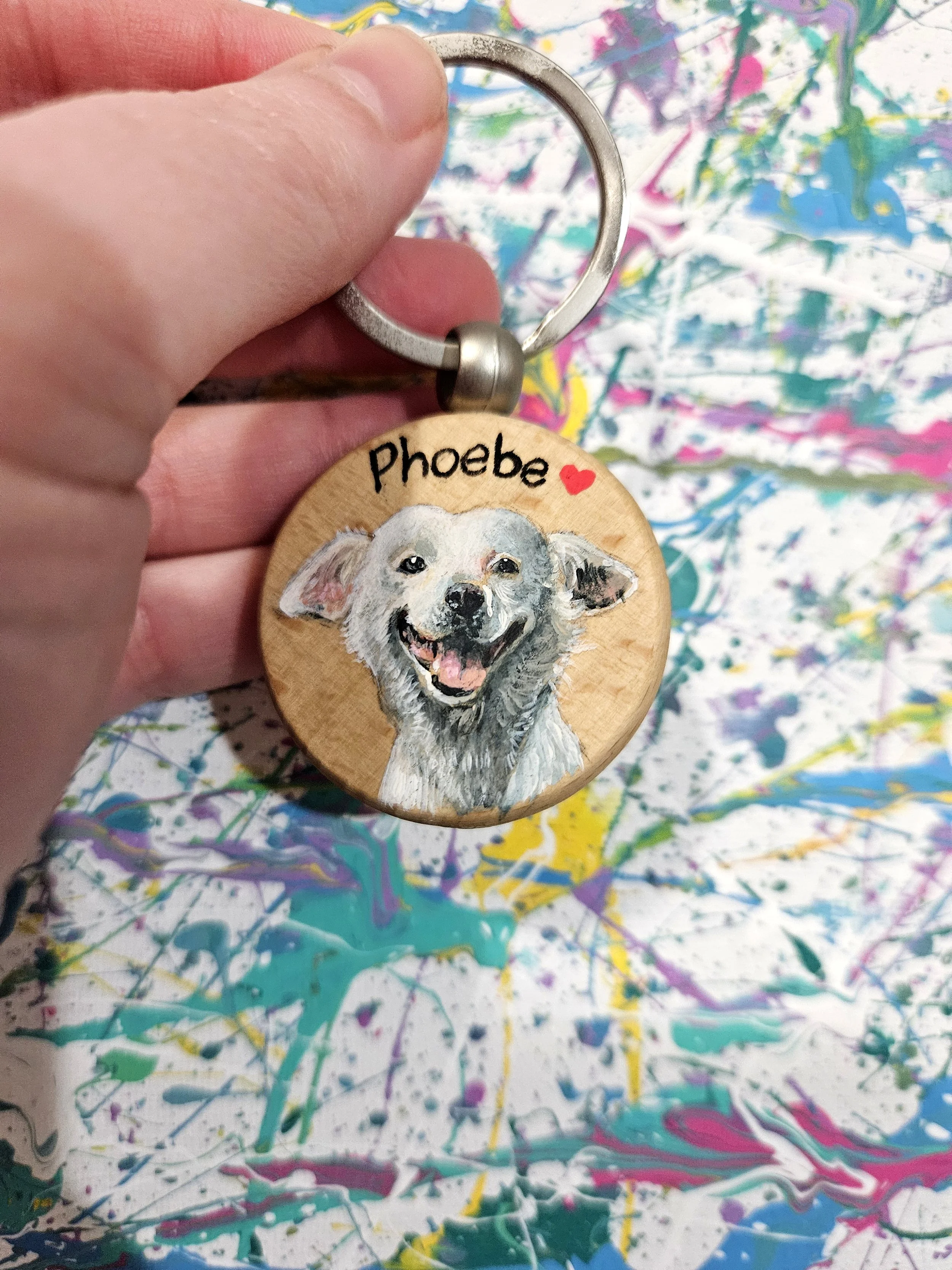 Hand holding a keychain with a circular wooden tag featuring a painted portrait of a dog and the name 'Nika' with a red heart.