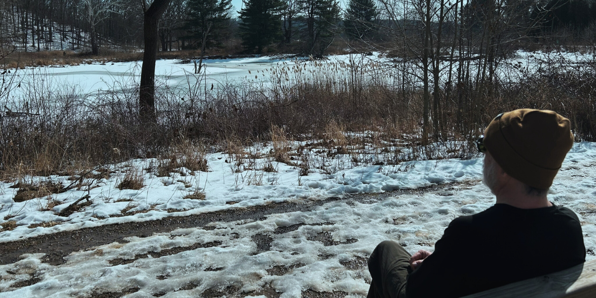 Leader sitting on a wooden bench during winter, looking out over a frozen pond and snow-covered field — symbolizing reflection during a quiet season.