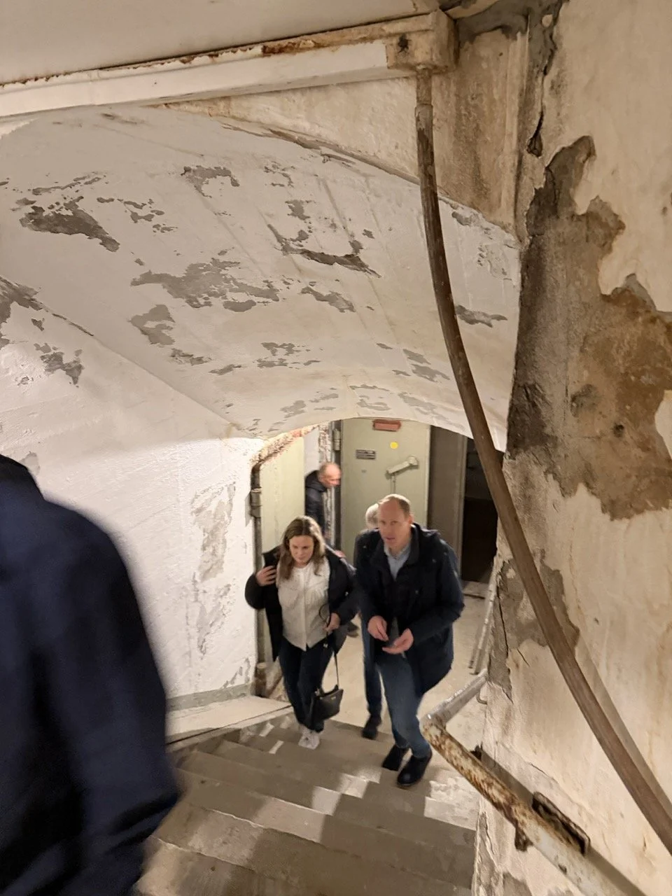 Mennesker går opp trapp i gammel, slitt bygning med skadde vegger.