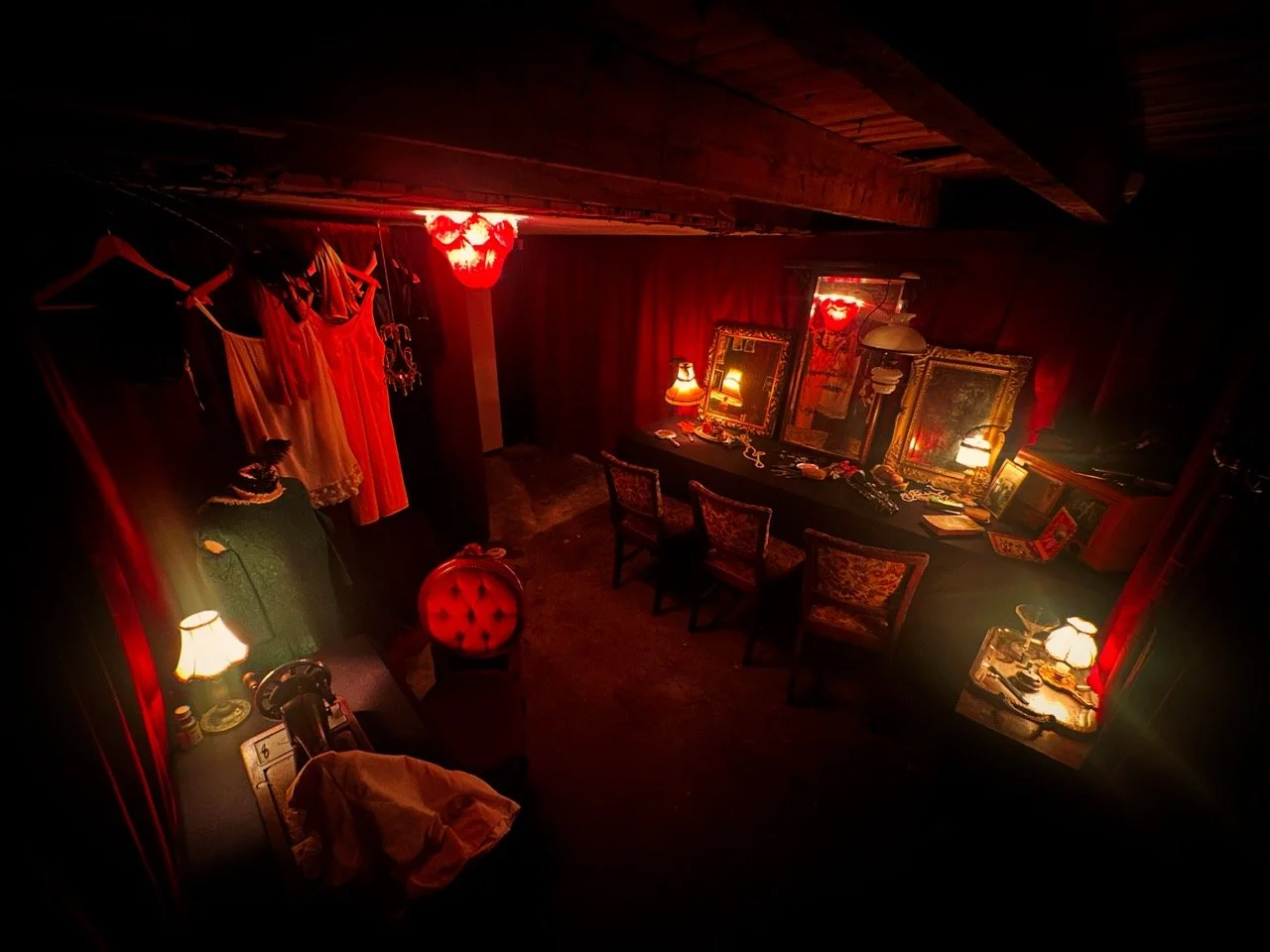 Et rom med rødt belysning, speil og antikke møbler, samt en hengende kjole og flere lamper.
