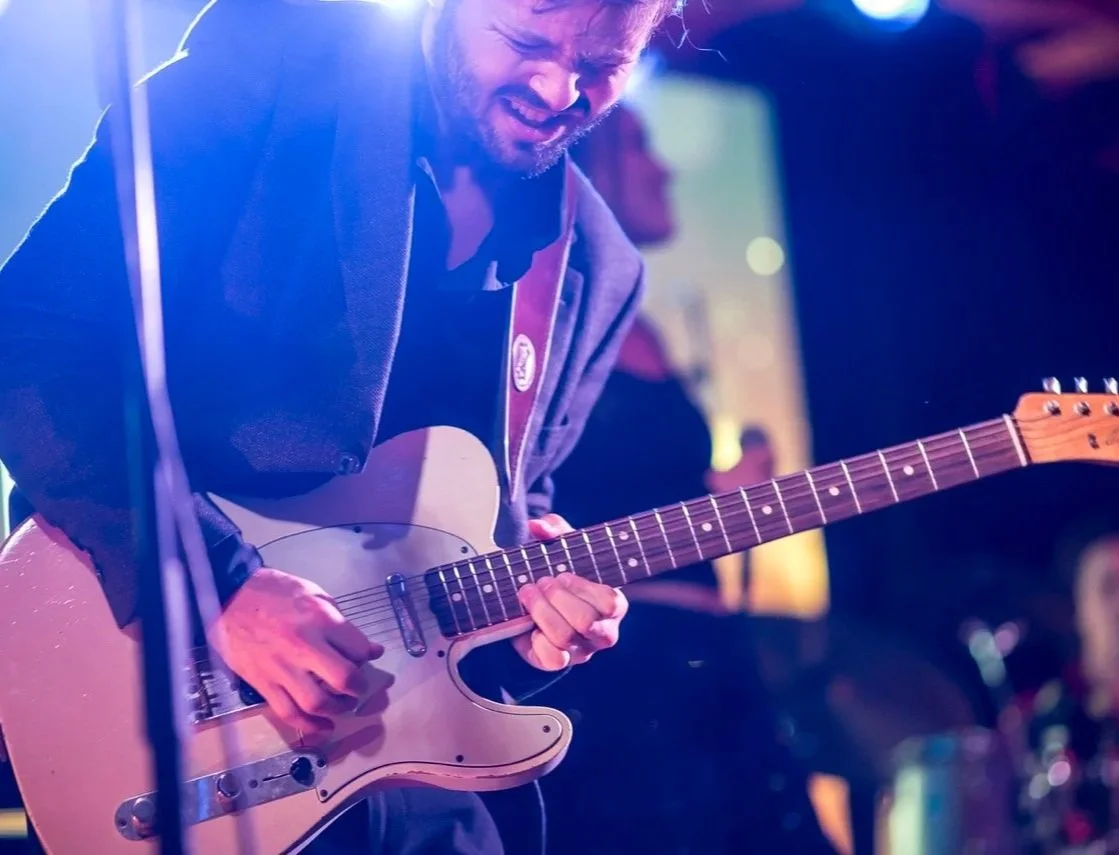En mann spiller elektrisk gitar under en konsert med fargerikt scenelys.
