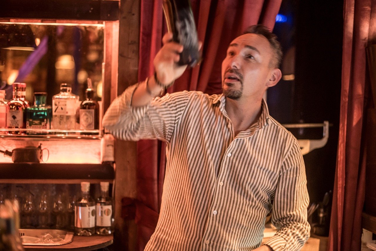 En mann med stripete skjorte som holder en flaske opp i en bar.