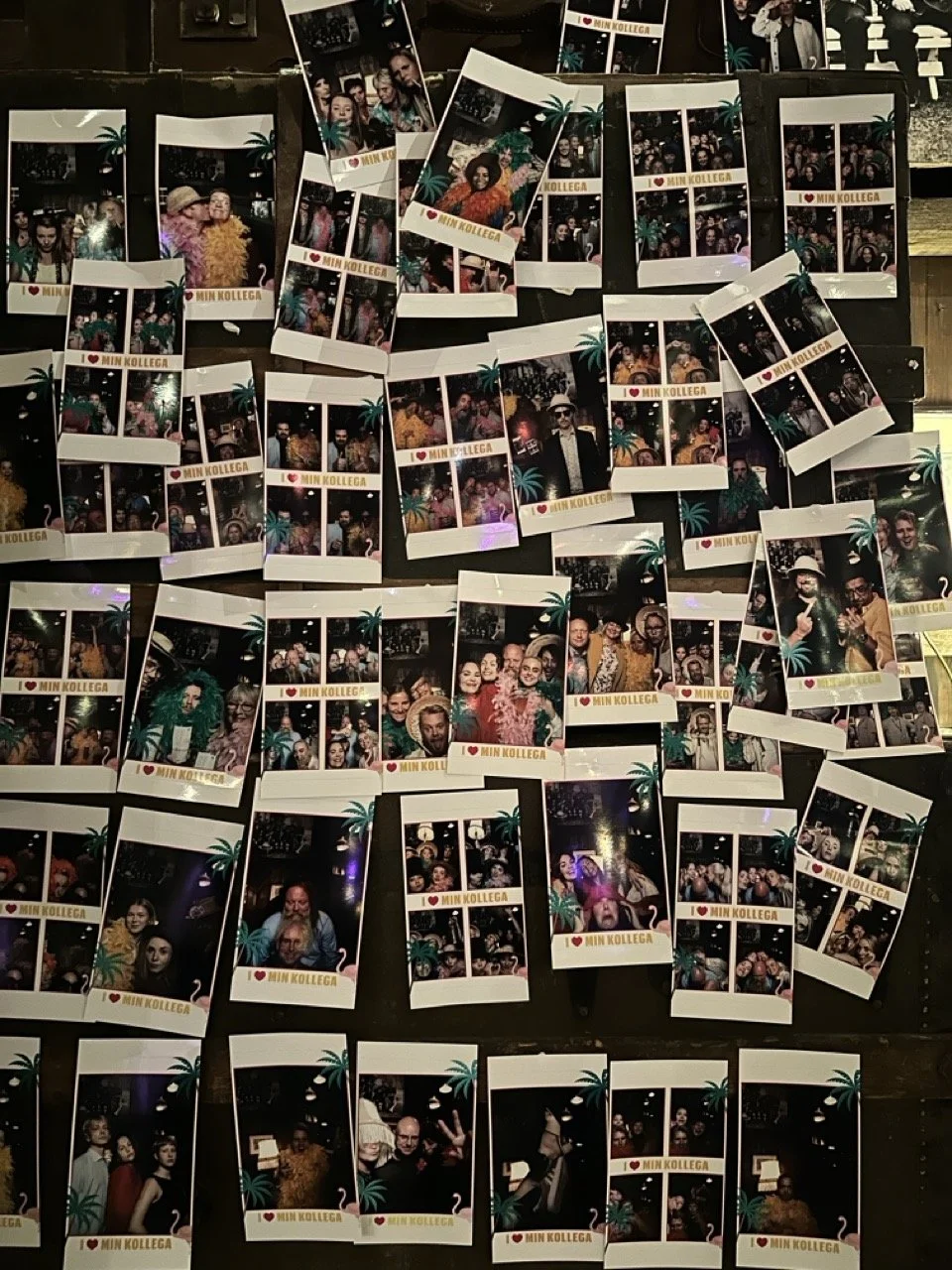 Fotografier av mennesker tatt i en fotoboks, med teksten 'I ❤️ Min Kollega', utstilt på en vegg.