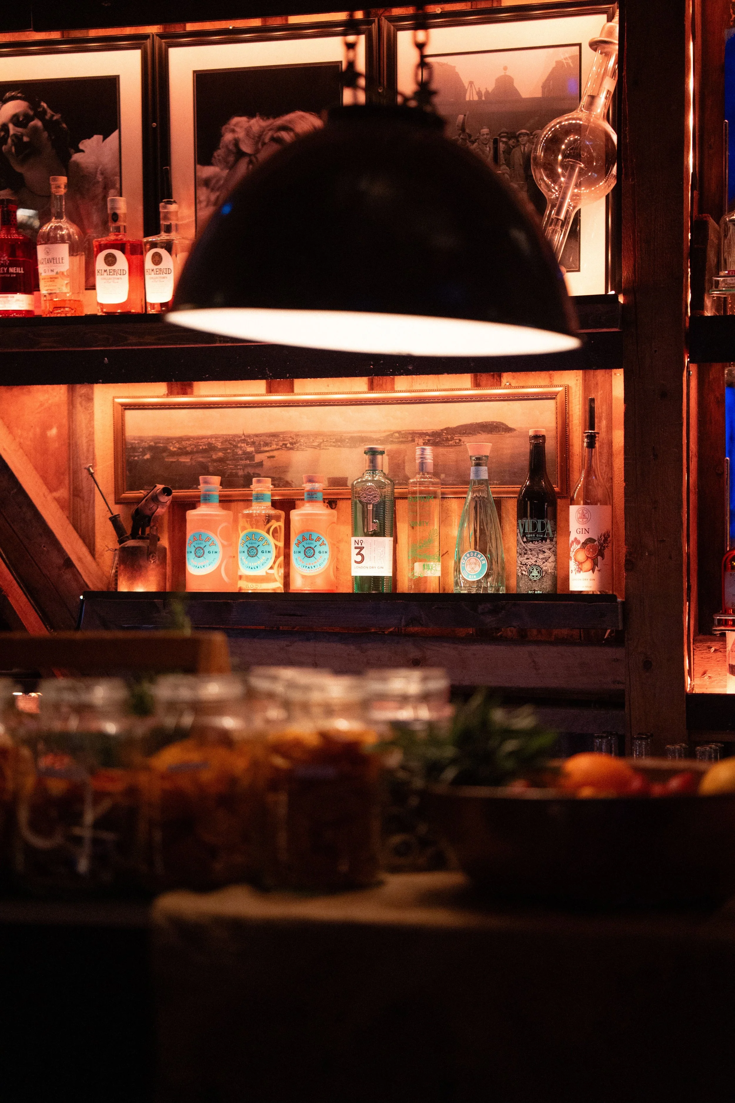 Et bar- eller restaurantinteriør med ulike alkoholflasker og bilder på veggen, sett fra lav vinkel.