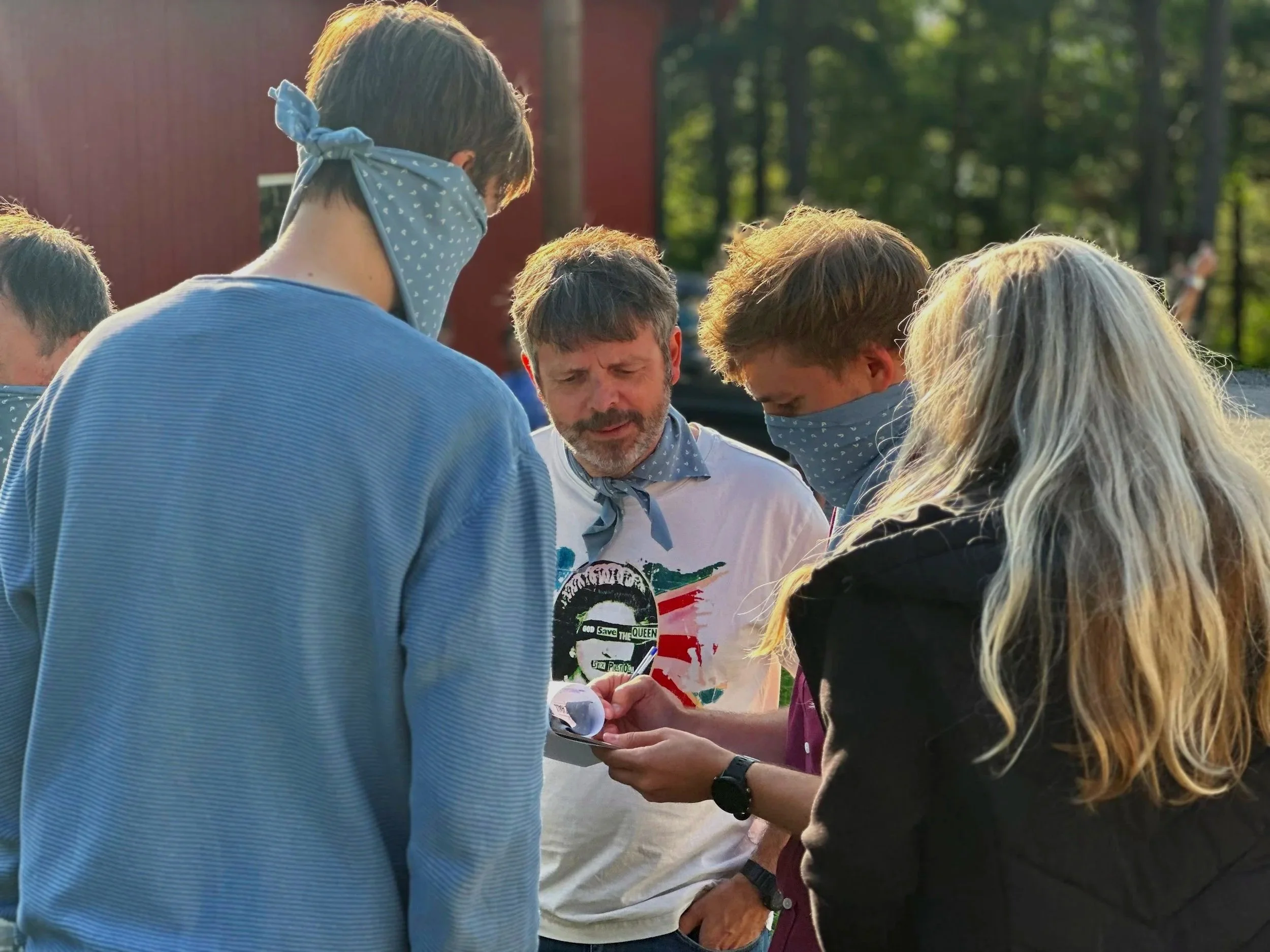 Gruppen mennesker som ser på en mobiltelefon utendørs, med noen personer som bruker masker.