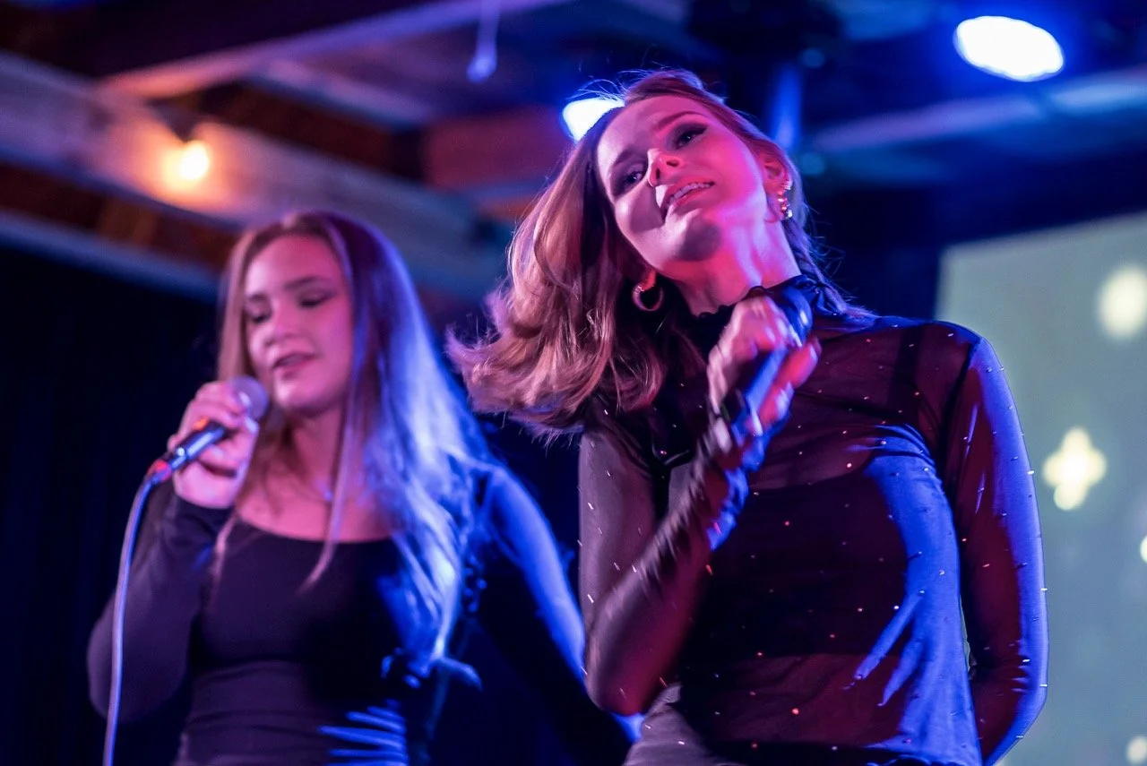 To kvinner synger på scenen med mikrofoner, under en konsert.