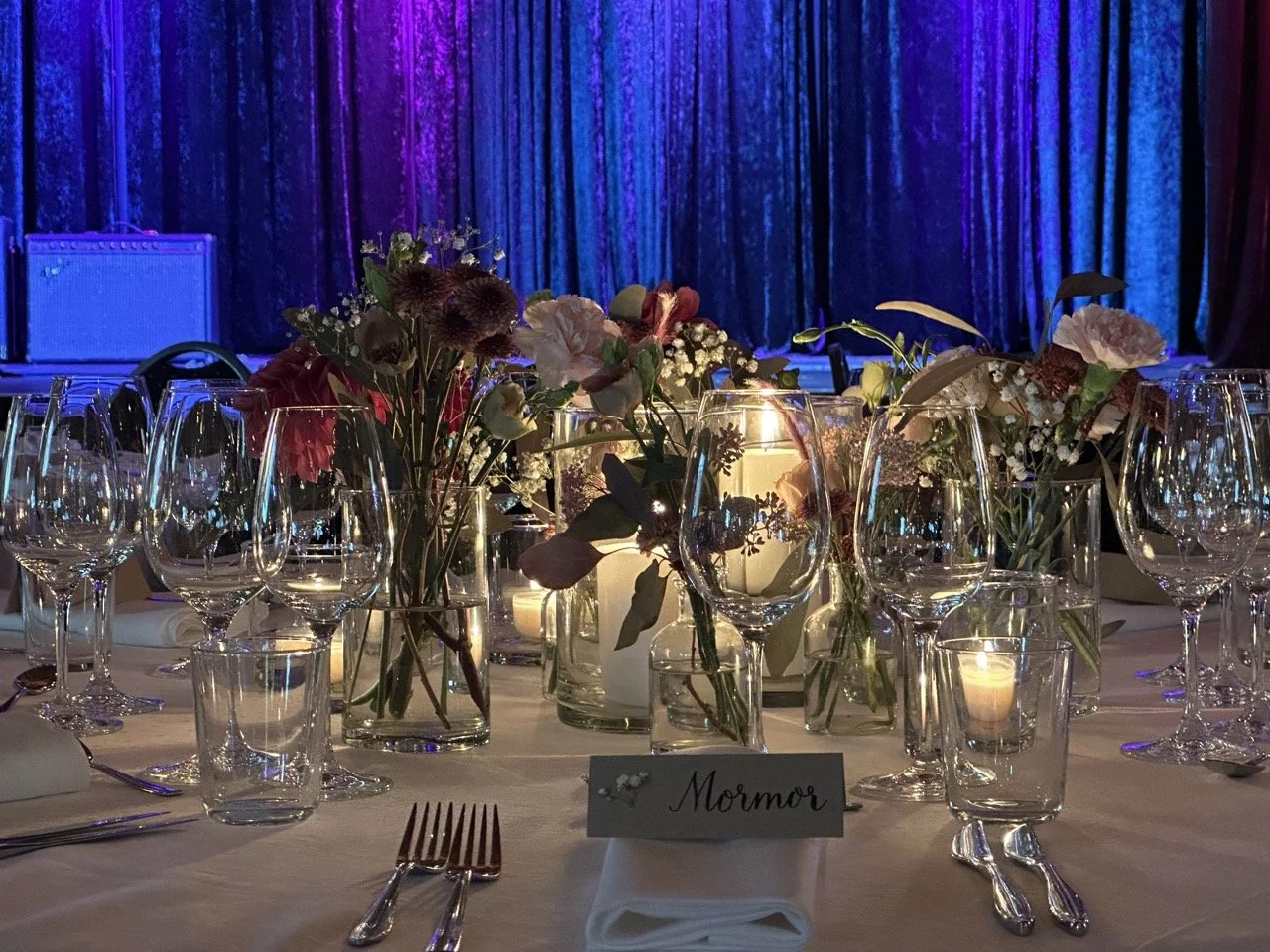 Dekket bord til en fest med blomsterdekorasjoner og lys på bordet, med blå og lilla belysning i bakgrunnen.