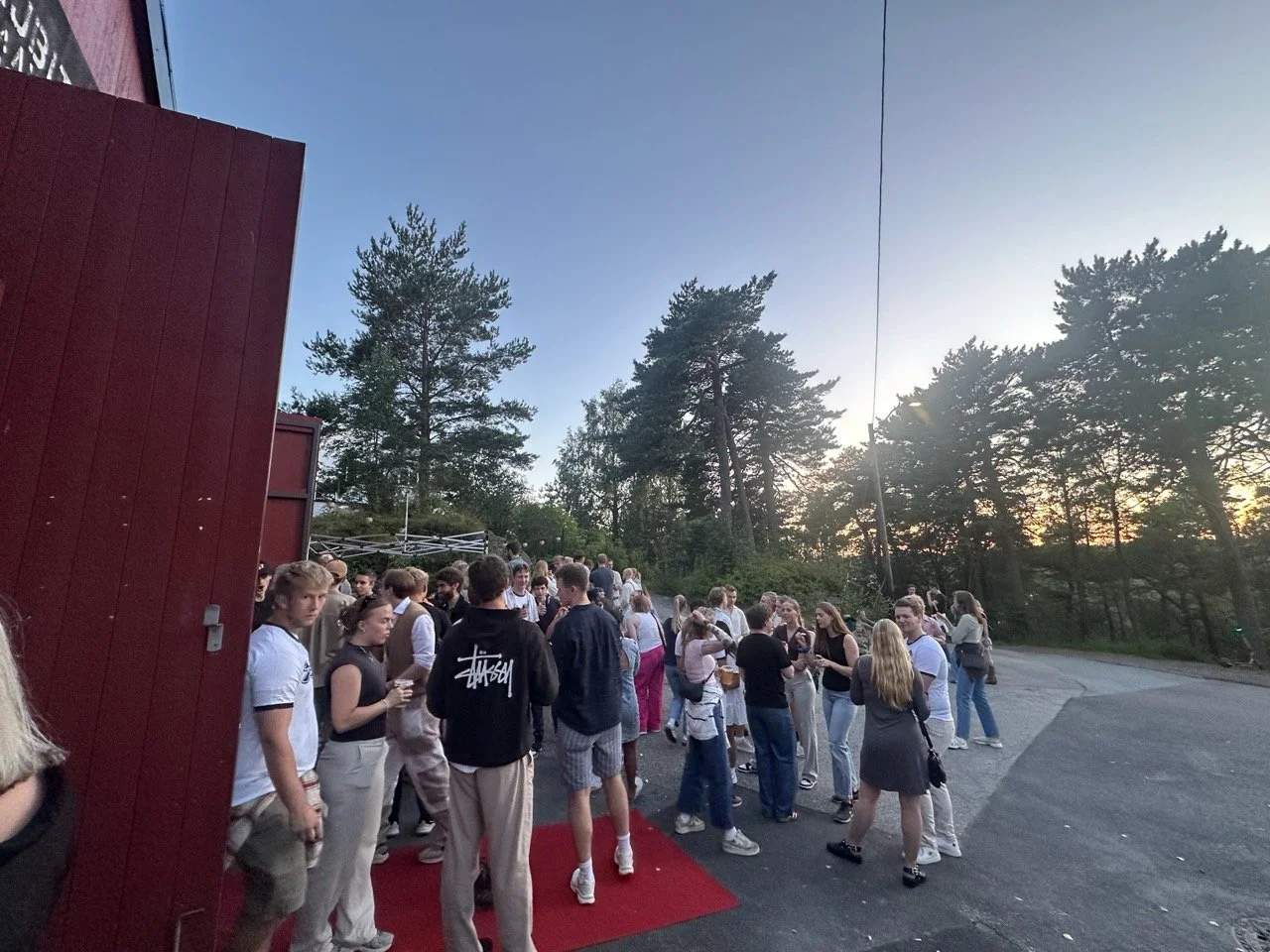 Gruppe med unge mennesker på en utendørs arrangement i skogen, med noen som står på en rød løper.