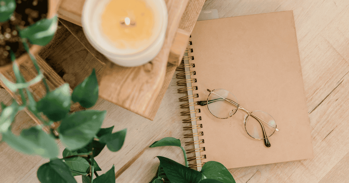 notebook on desk with glasses, a candle, and plant